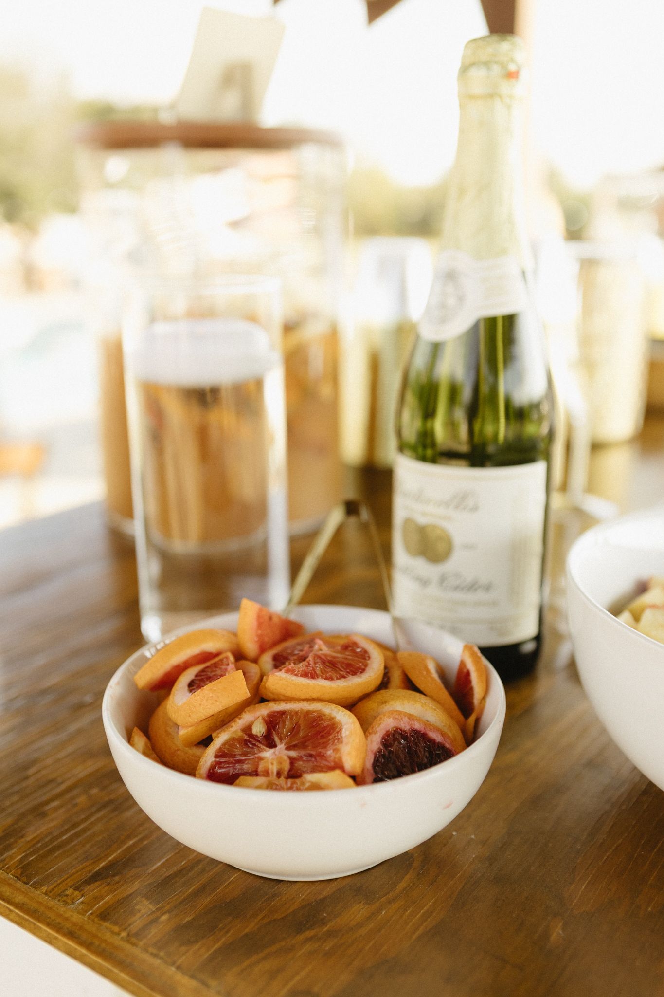 Wine bottles and appetizer plates displayed on a rustic wooden table at an outdoor event.