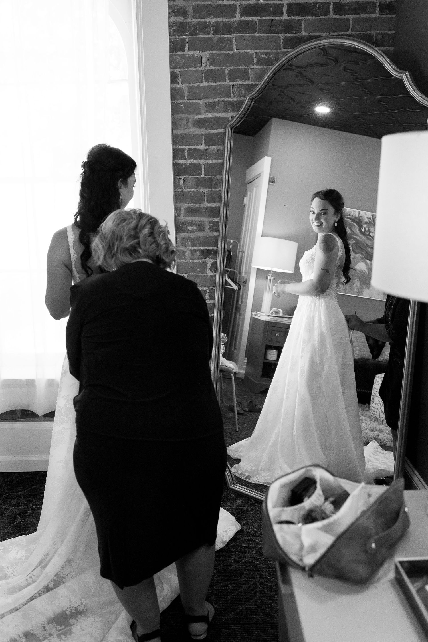 A bride gets ready in a room with exposed brick walls as helpers assist with final preparations.