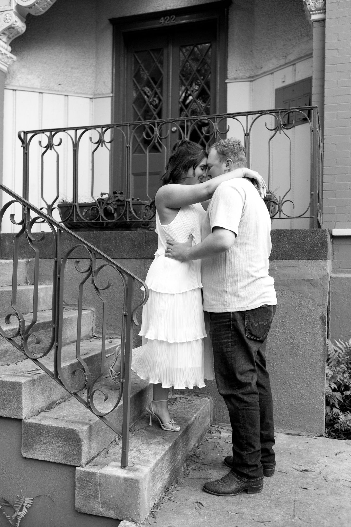 A black and white photograph of an intimate moment on historic steps with decorative iron railings.