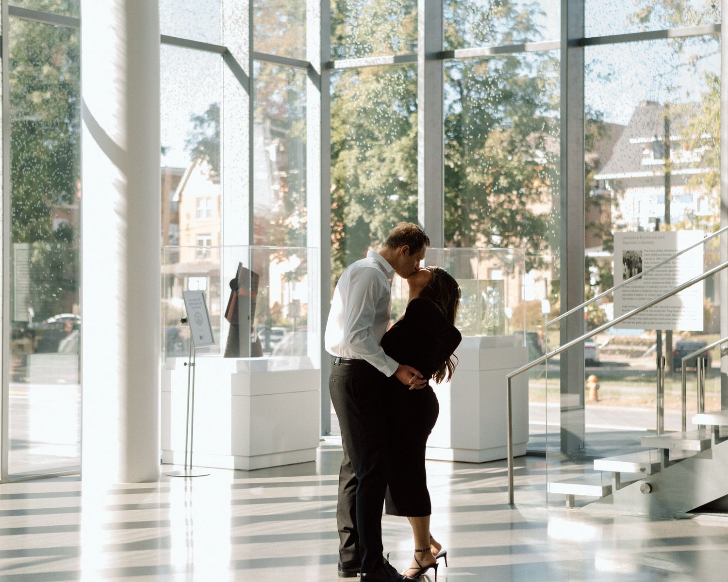 Engaged couple in downtown Louisville, with the woman smiling and showing her engagement ring while embracing her fiancé