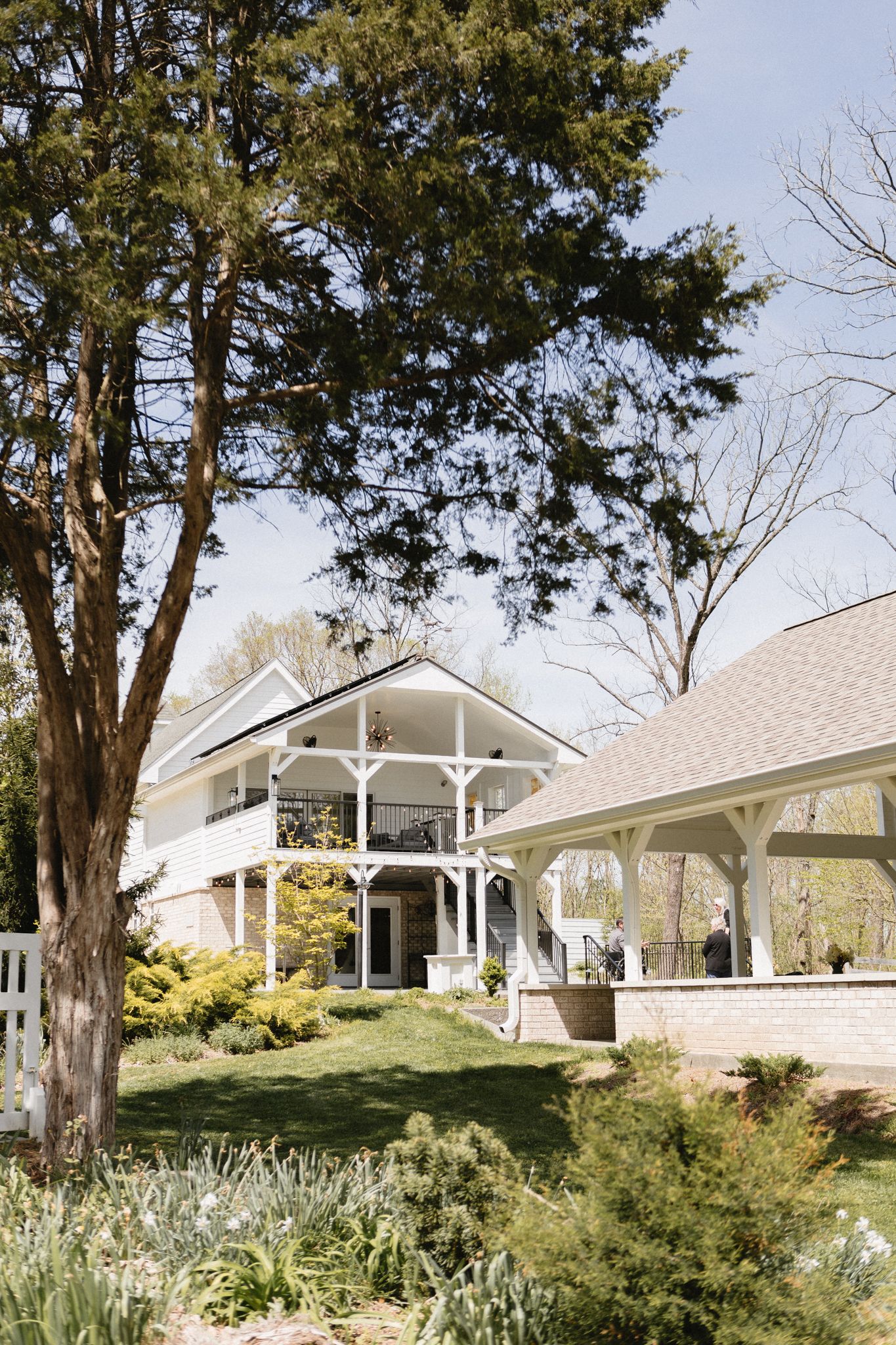 Elegant white Victorian-style wedding venue with ornate wraparound porch and lush landscaping on a sunny spring day.