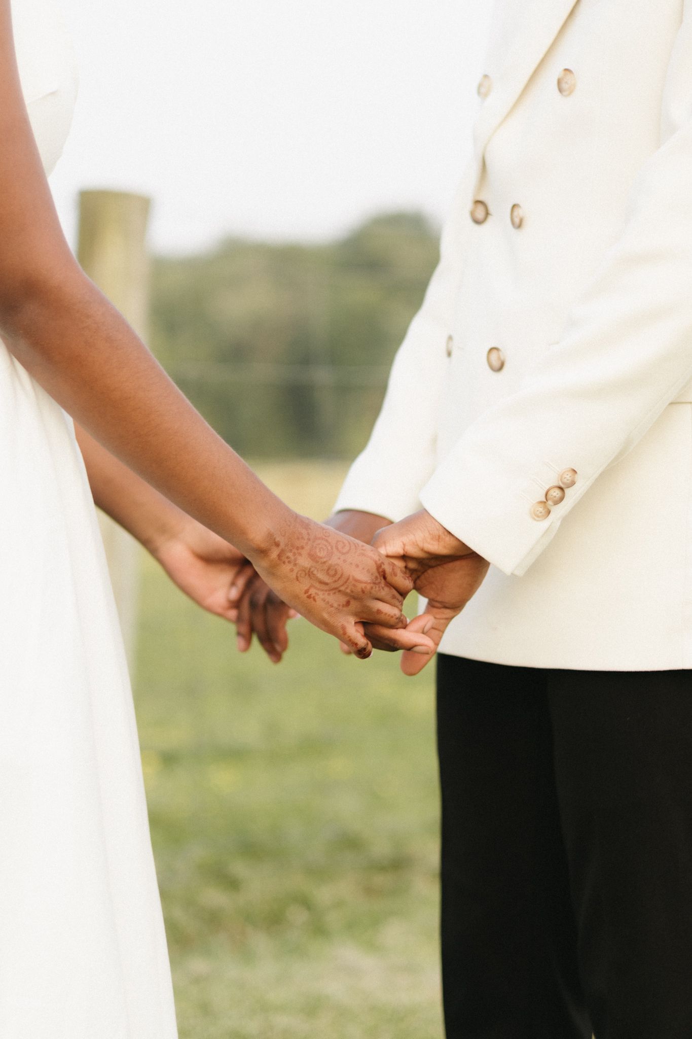 Close up of a couple holding hands, showing white wedding attire details.