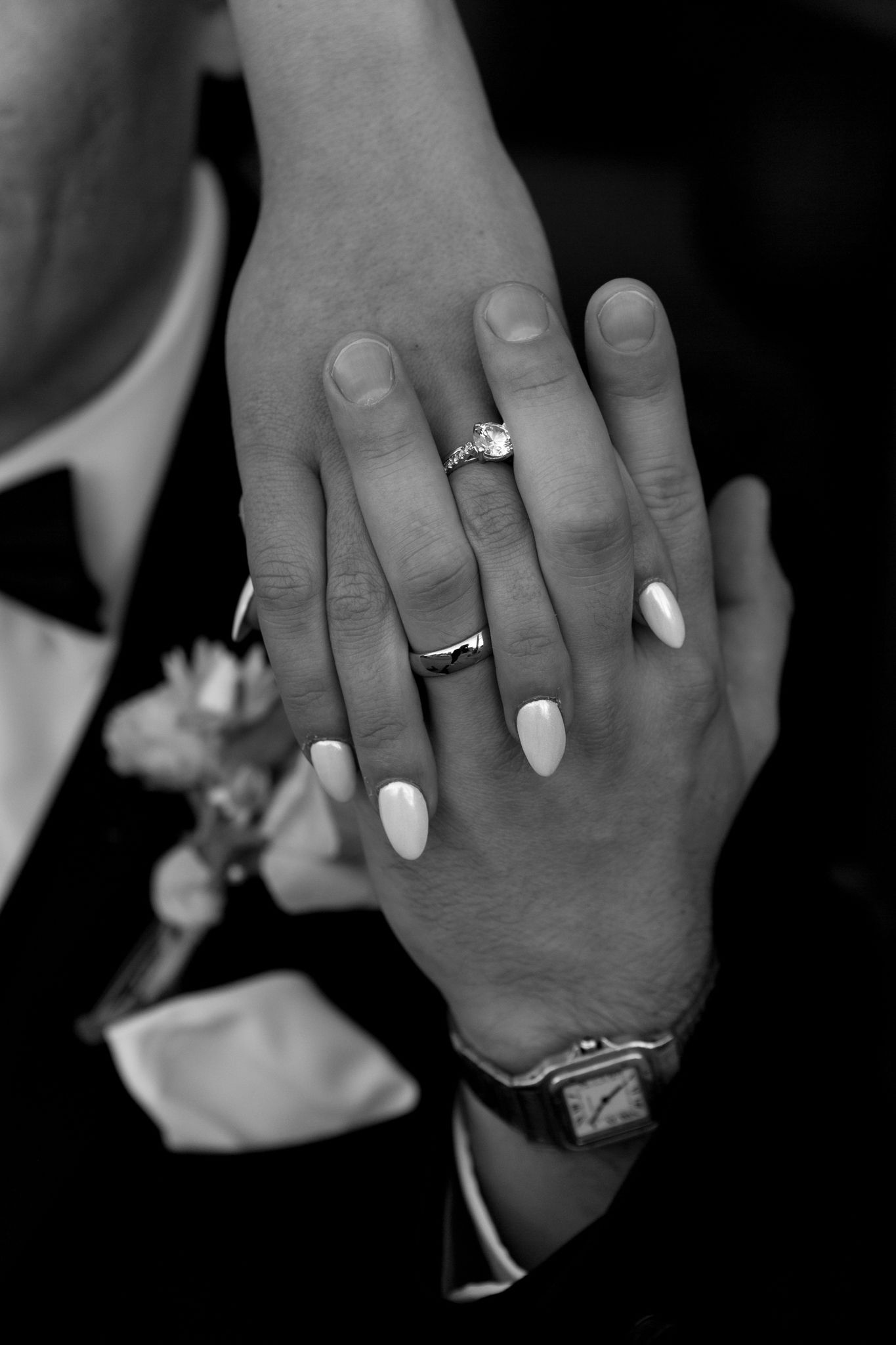 Close-up black and white photo of hands with wedding rings and a white manicure.