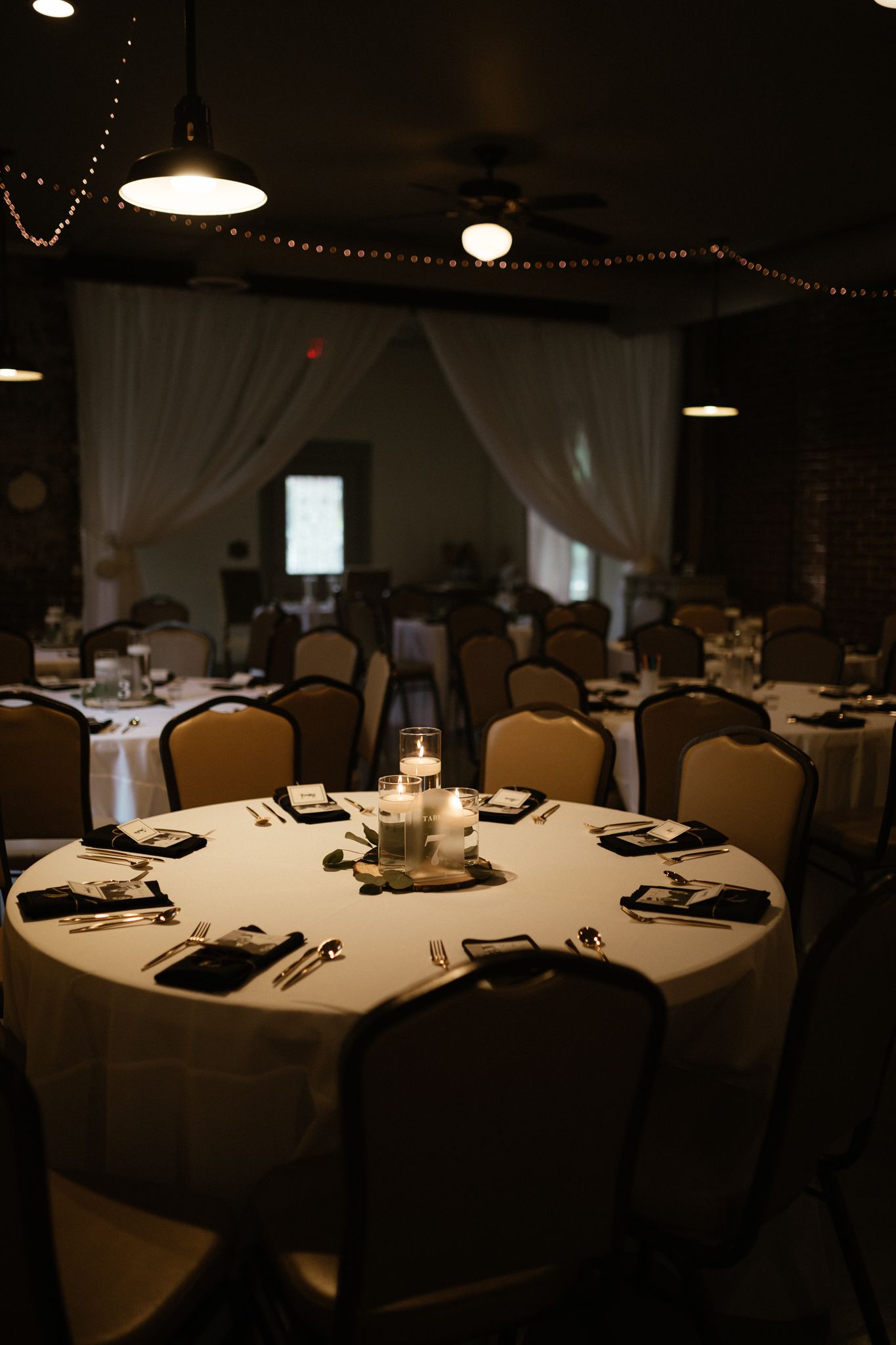 Elegantly set round banquet table with white linens and centerpiece candle in a dimly lit reception venue.