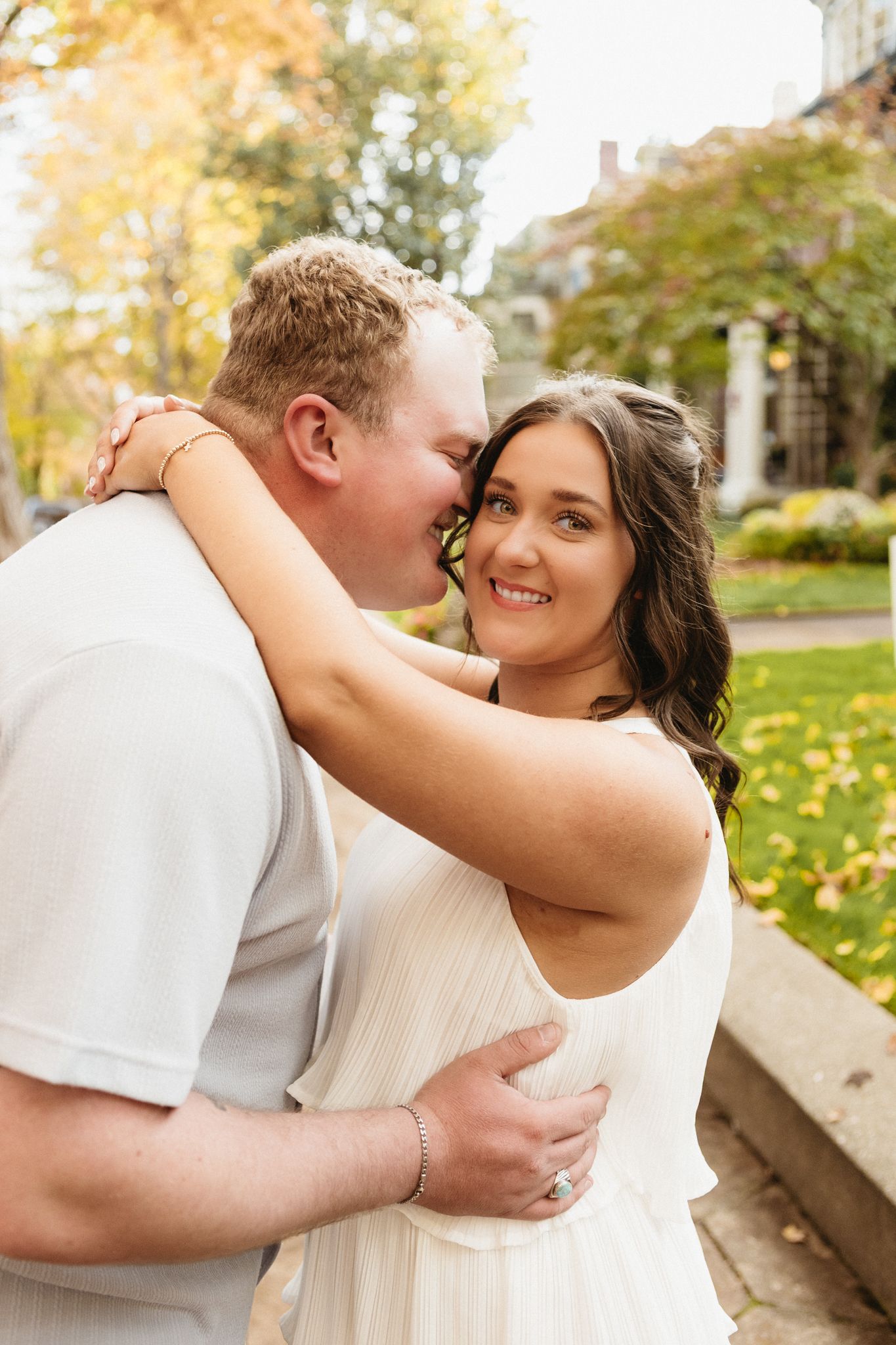 A couple in wedding attire share romantic moments in an outdoor autumn setting with fallen leaves.