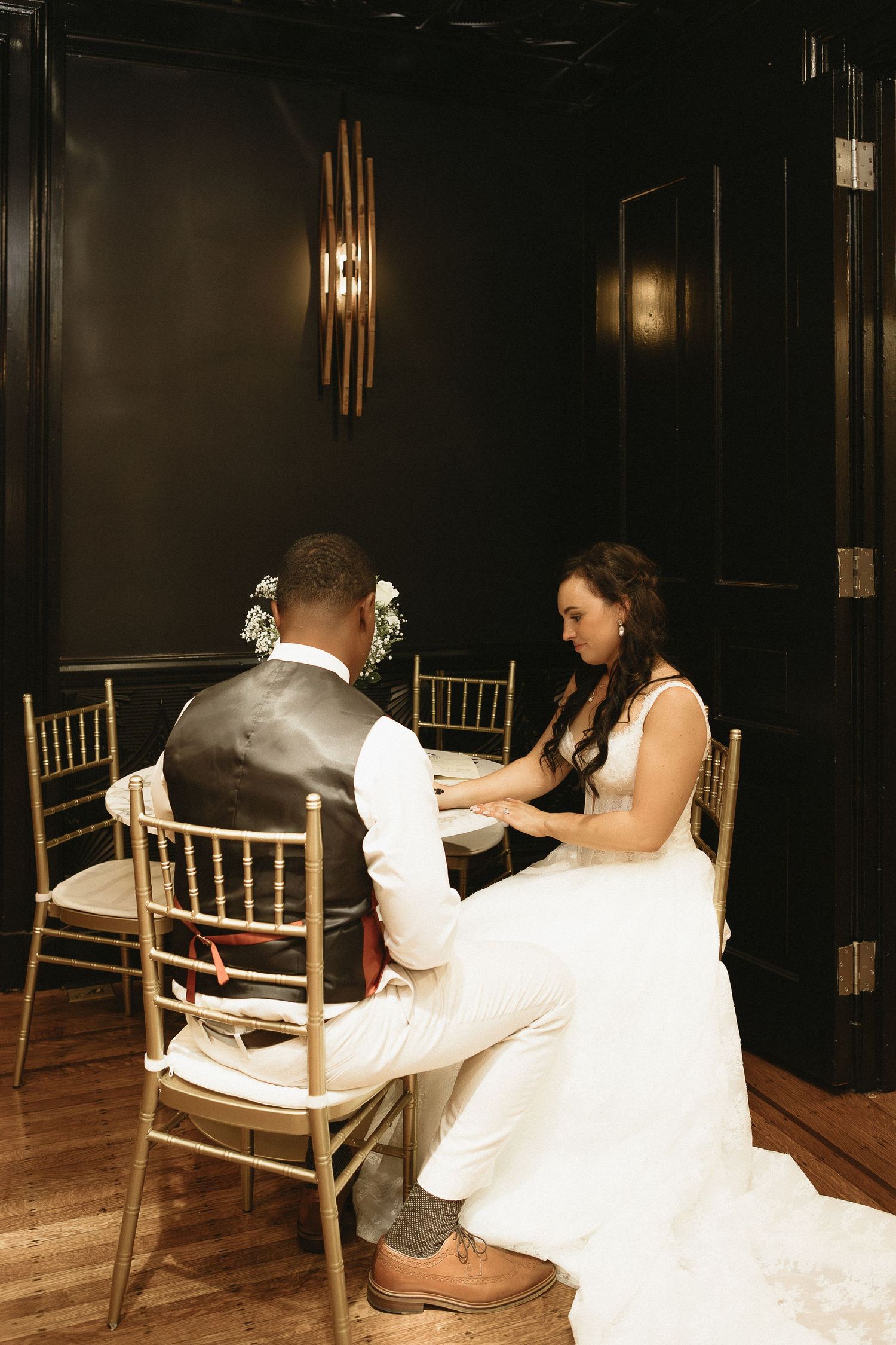 Intimate moment between couple in elegant venue with gold chairs and dark walls.