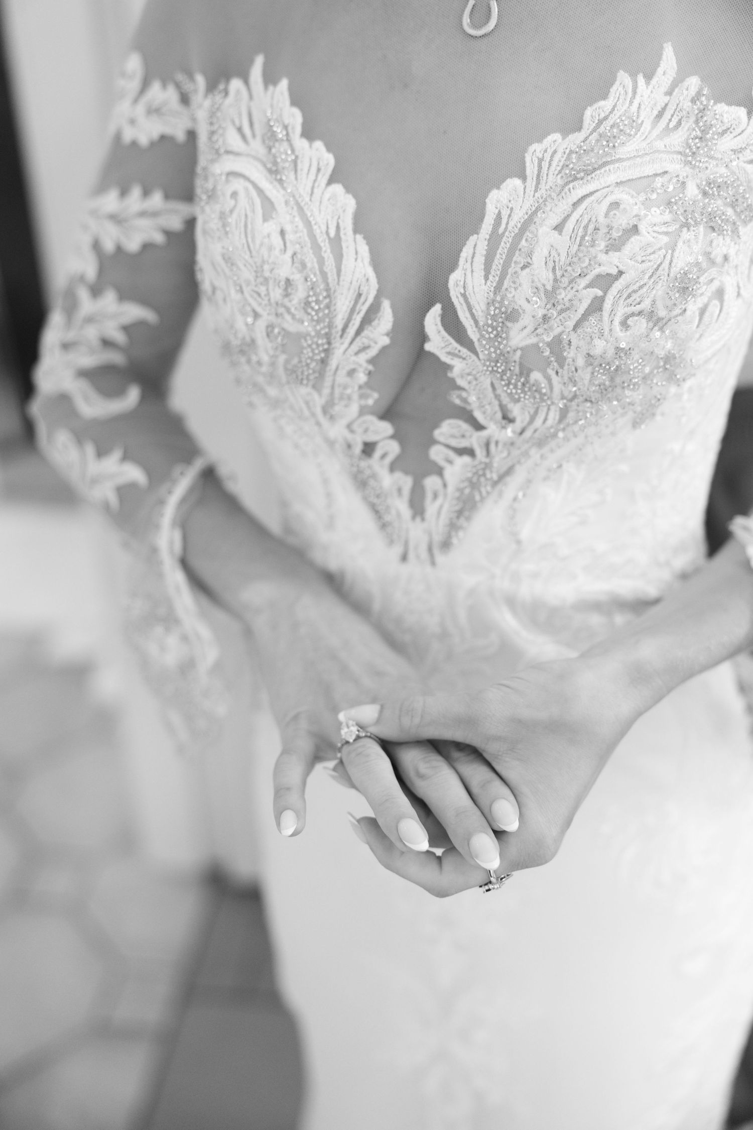 Close-up of a bride in an intricate lace wedding gown with clasped hands showing an engagement ring.