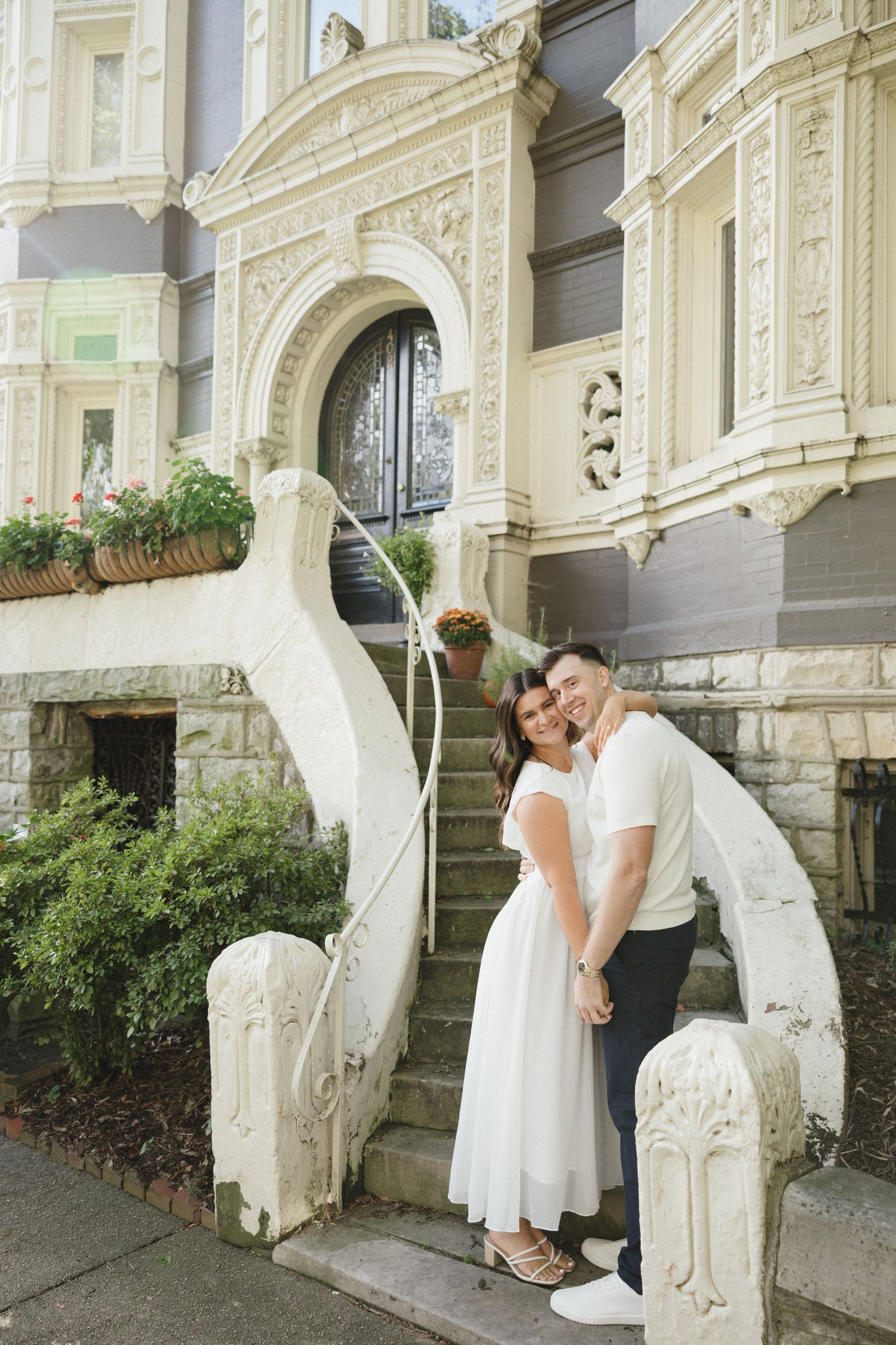 Couple standing together at the base of decorative white stone steps of a historic ornate building.