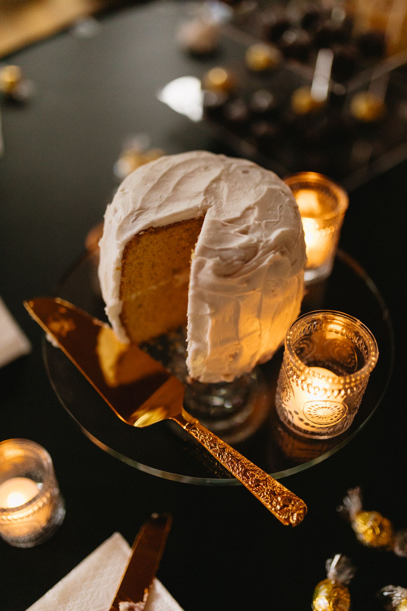 white wedding cake surrounded by small candle lights and gold candy