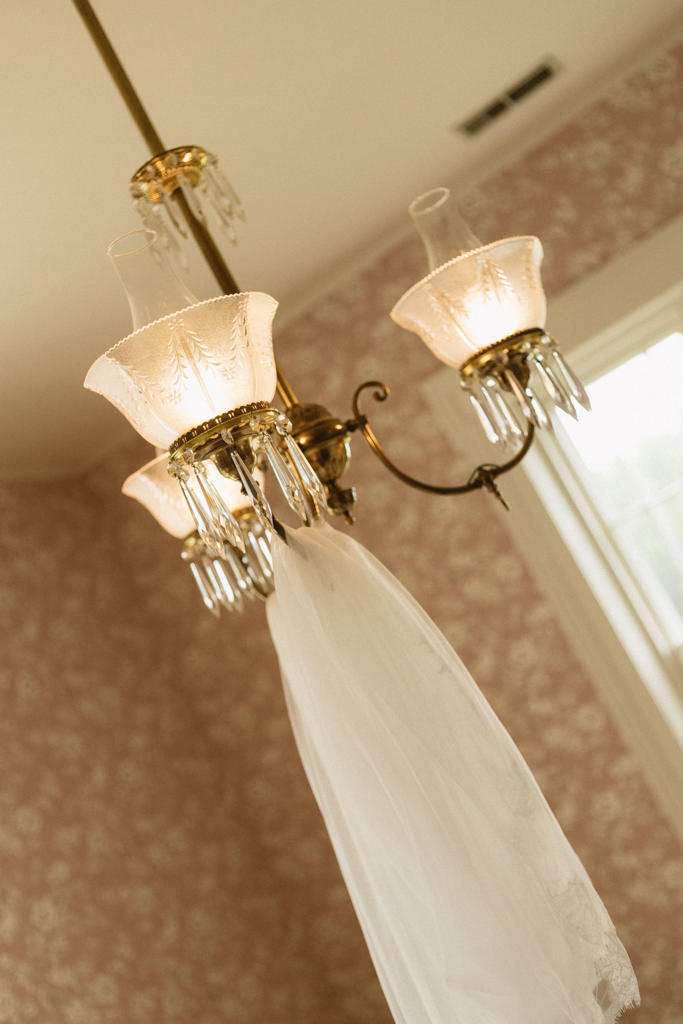 A crystal chandelier with frosted glass shades hangs elegantly from a textured ceiling with ornate wall patterns.