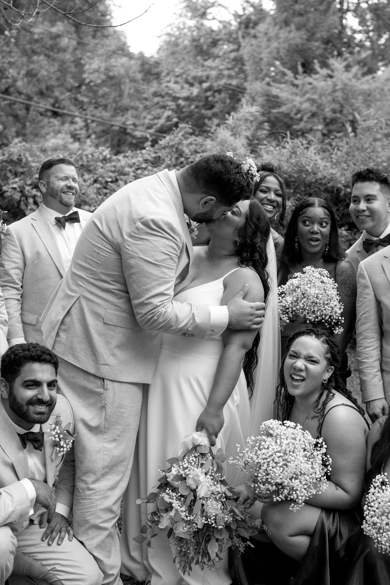 A joyous moment captured in black and white as a wedding party laughs together during outdoor formal photos.