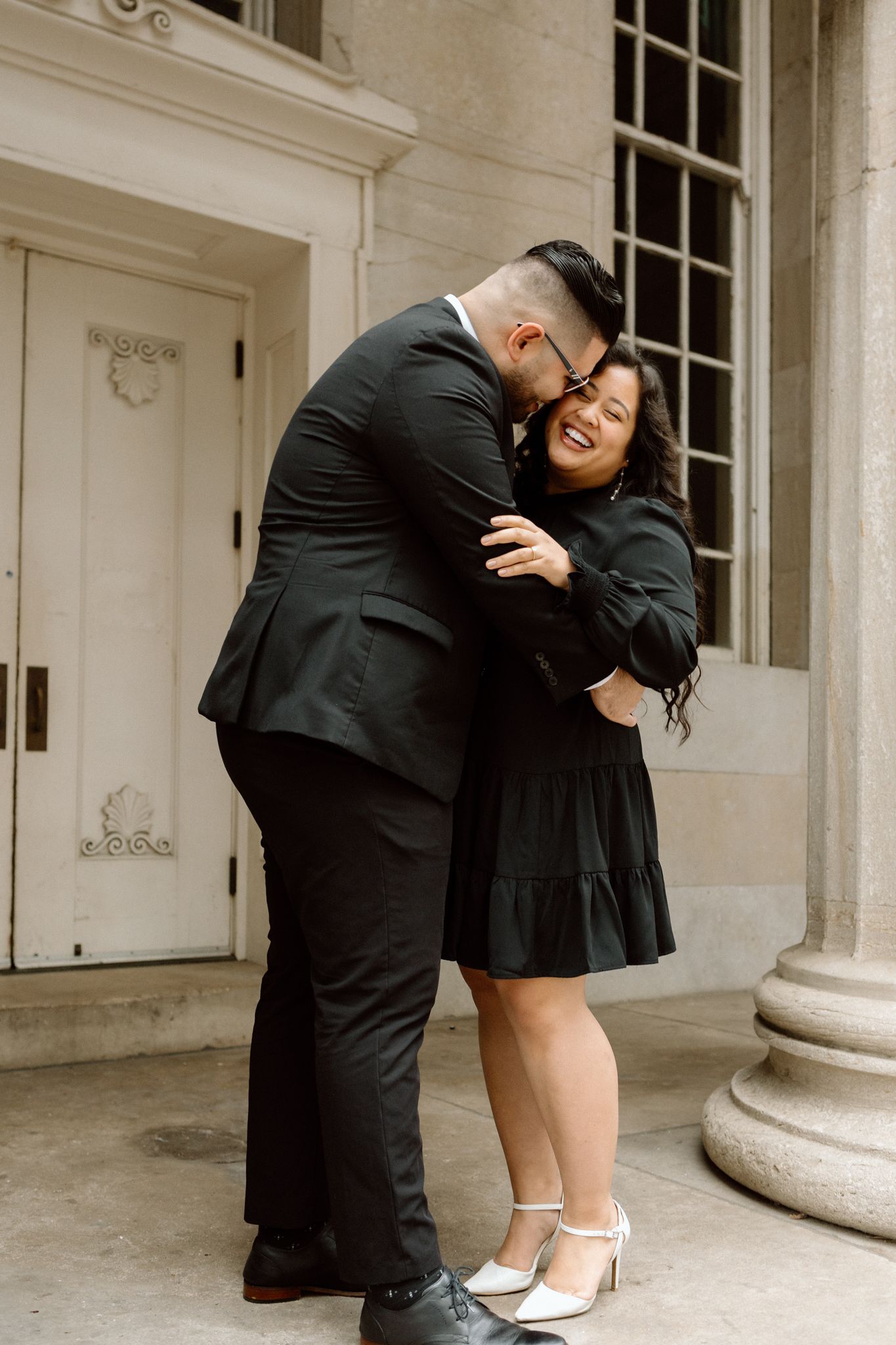 Engaged couple in downtown Louisville, with the woman smiling and showing her engagement ring while embracing her fiancé