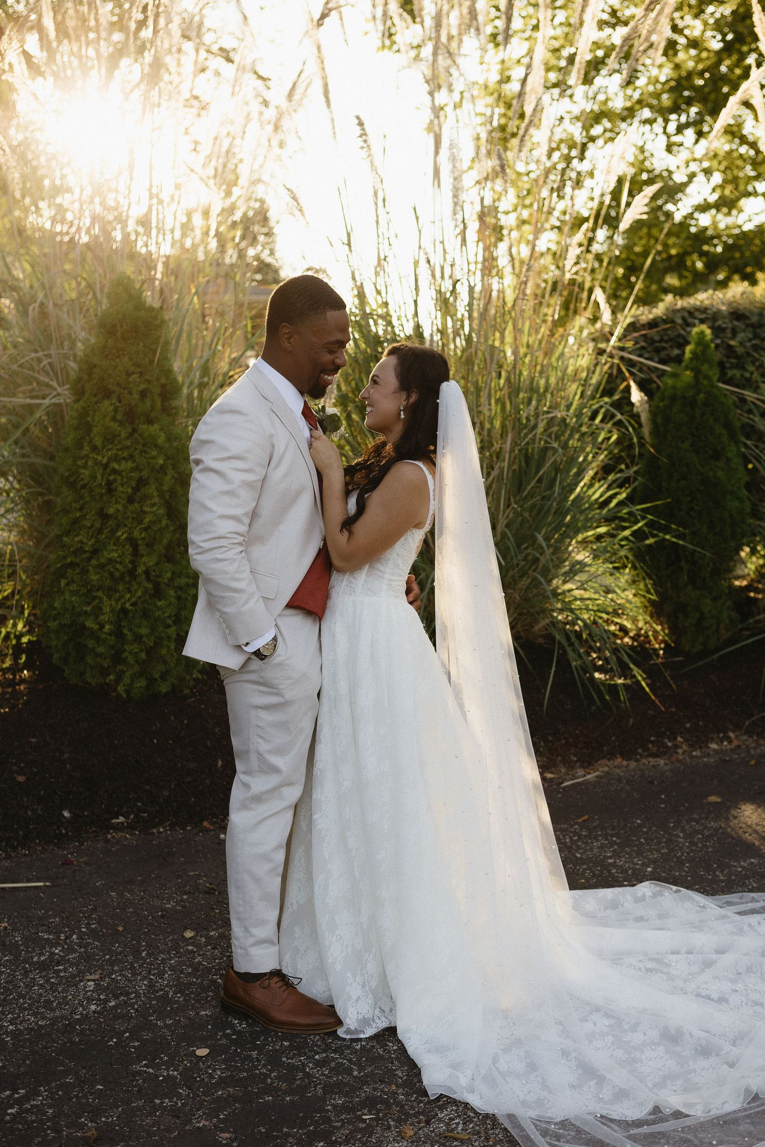A romantic sunset wedding photo of a couple embracing among tall ornamental grasses.