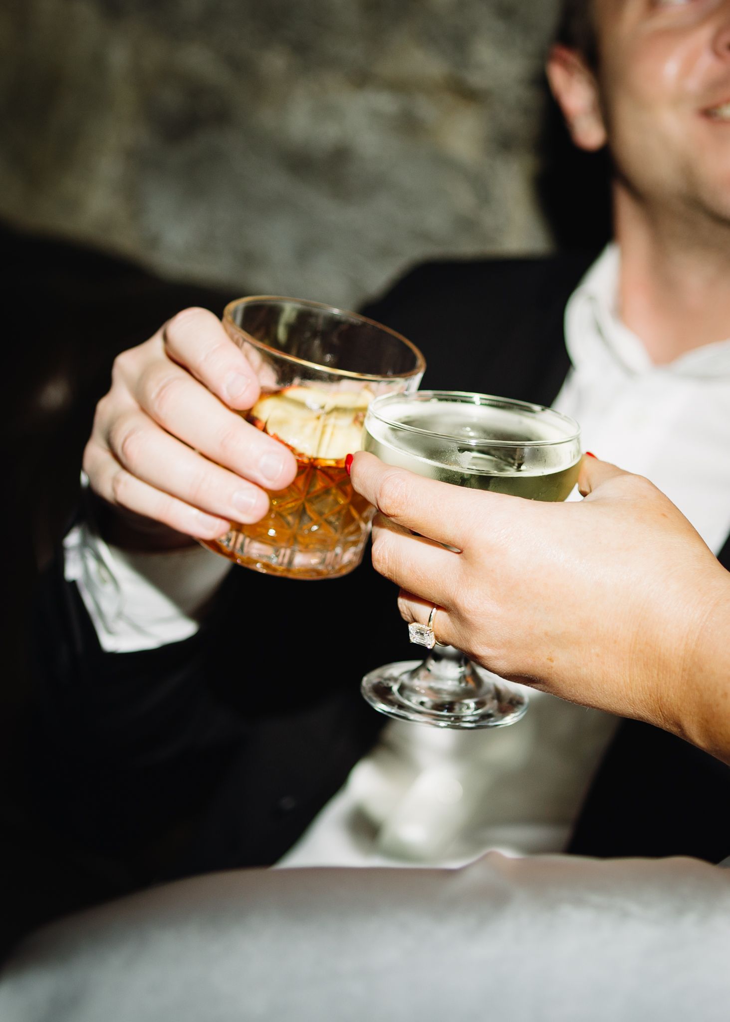 Two hands toasting with cocktail glasses at an evening gathering.