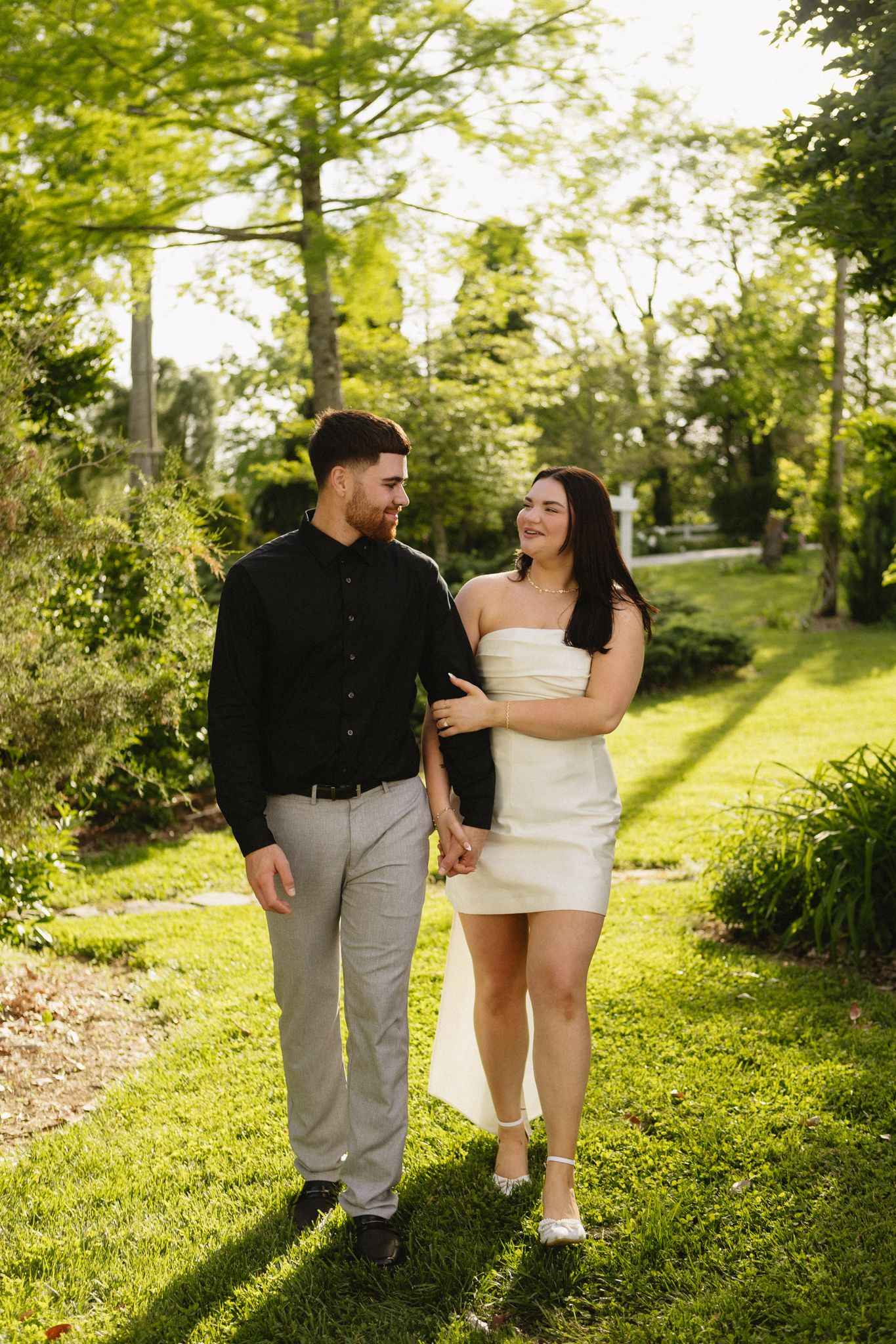 A couple strolling and laughing together on a lush green lawn during golden hour.