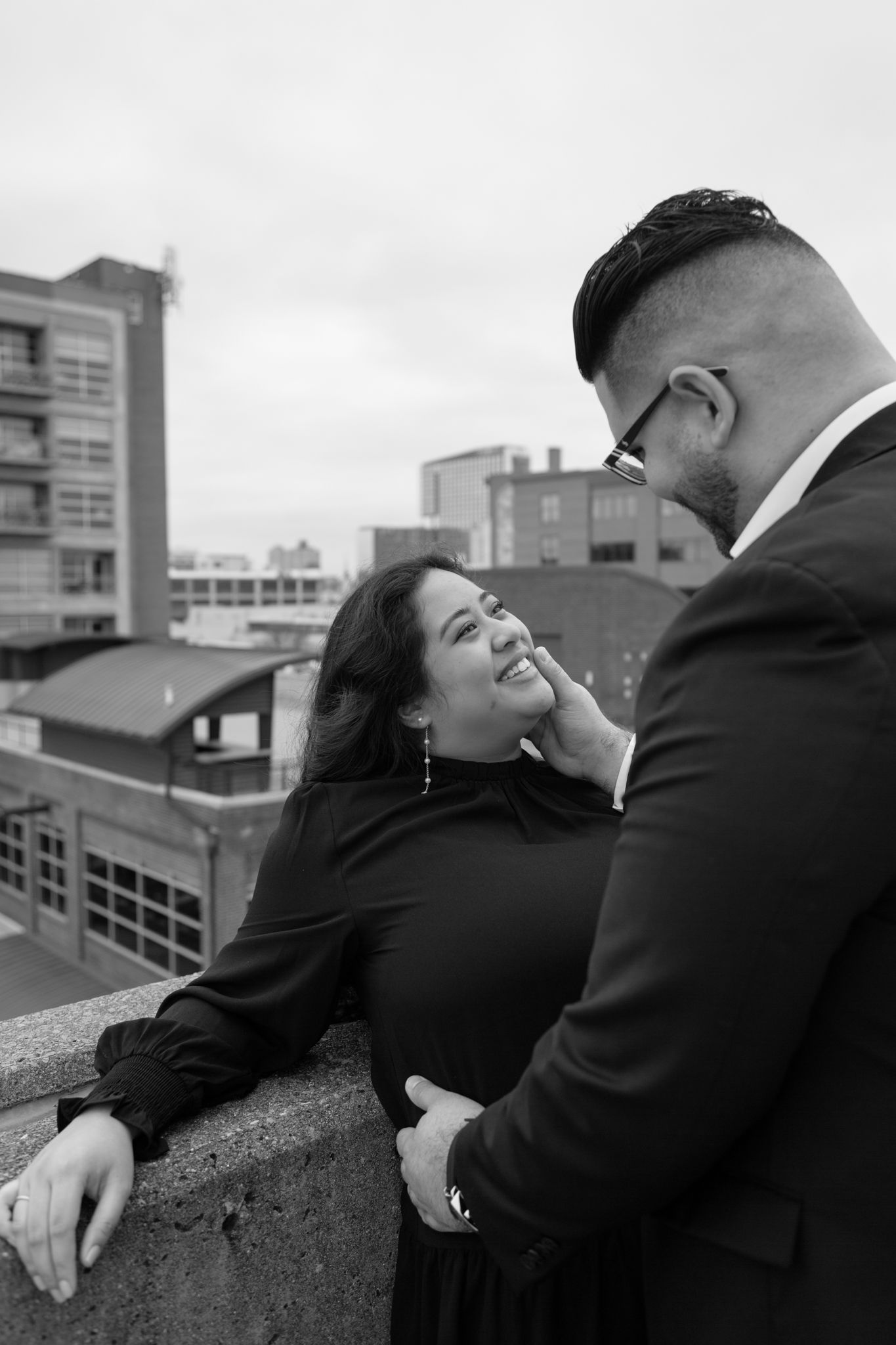Elegant engaged couple smiling and embracing in downtown Louisville, with the woman showing her engagement ring