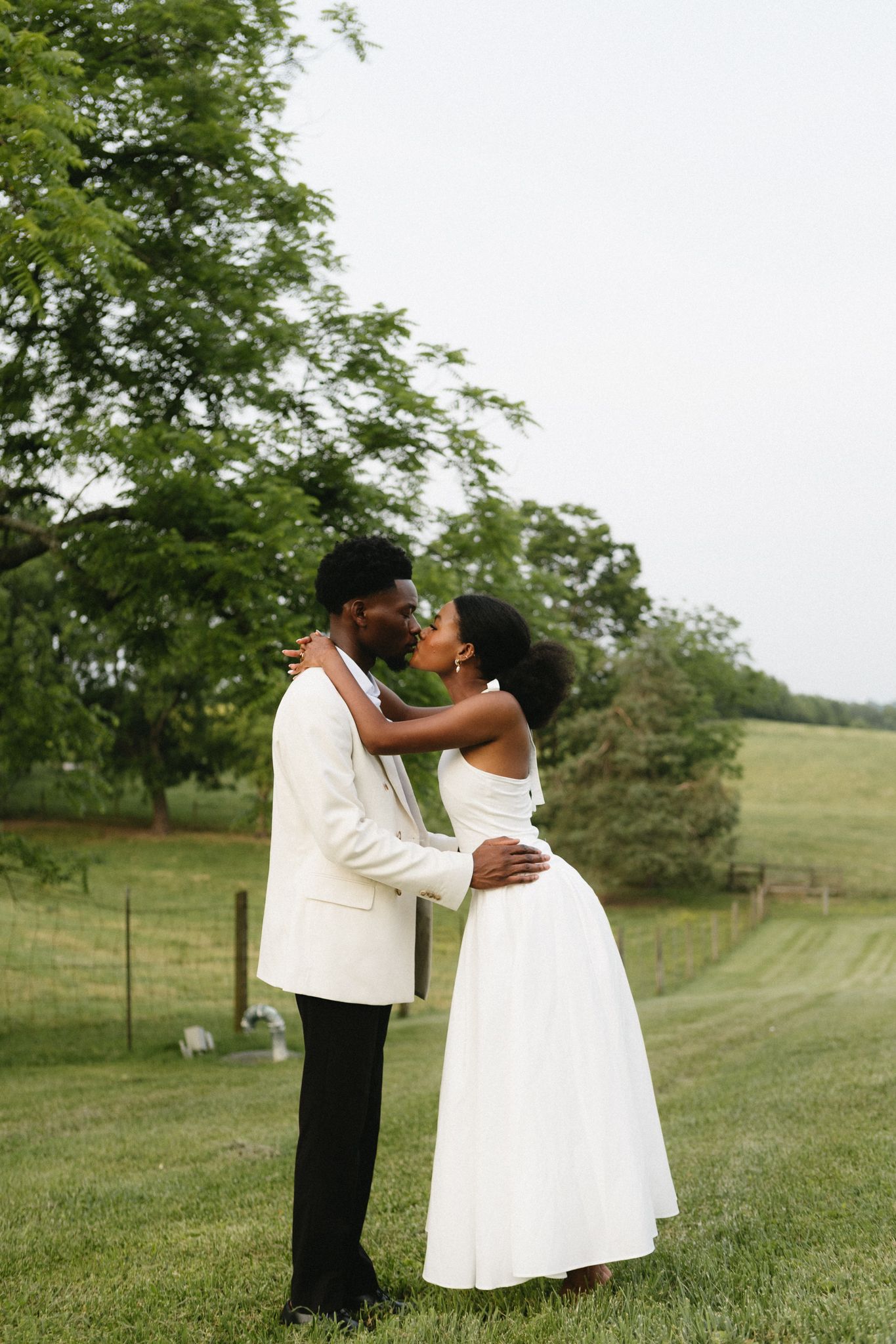 Newlyweds share intimate moments in a scenic green countryside setting.