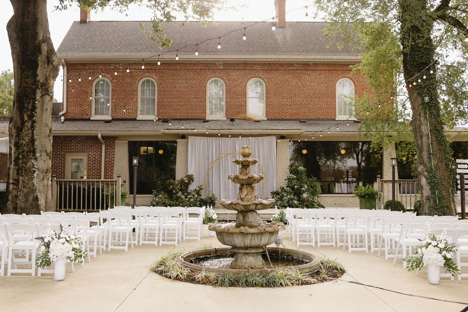 Outdoor wedding venue with white chairs arranged for ceremony under mature trees.