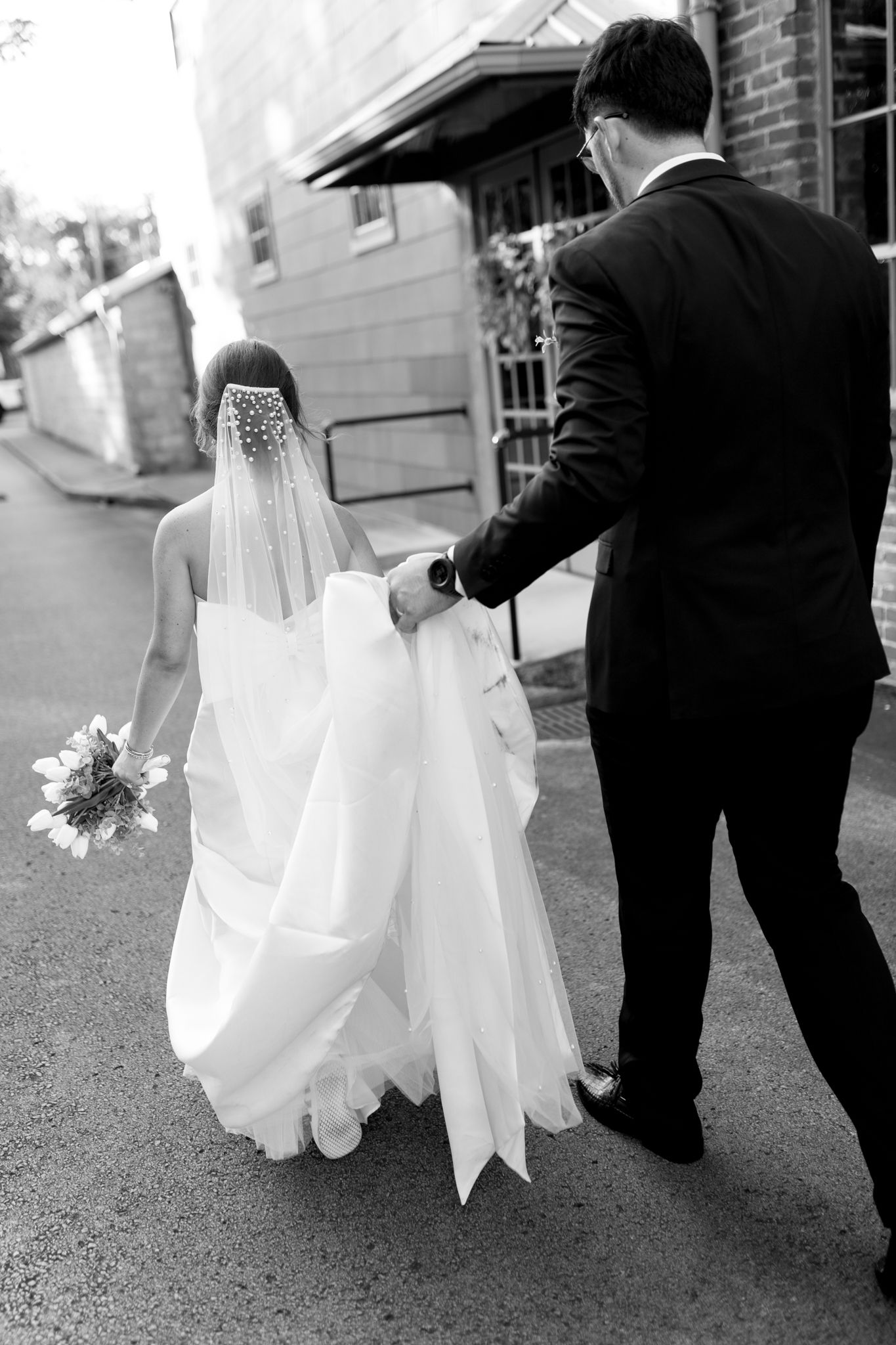 Black and white photo of wedding dress train being arranged on pavement.