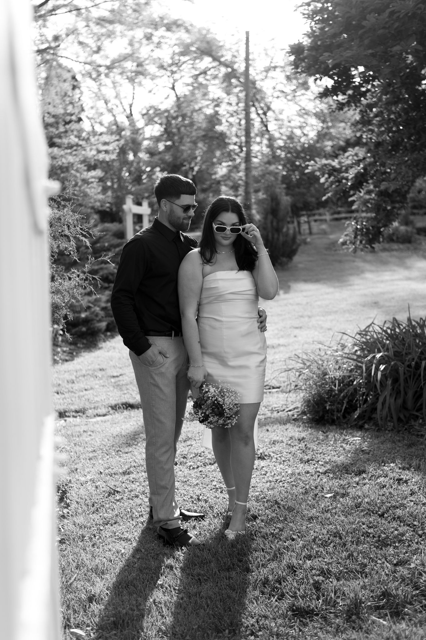 A black and white photo of couple walking together in a garden with long shadows on the ground.