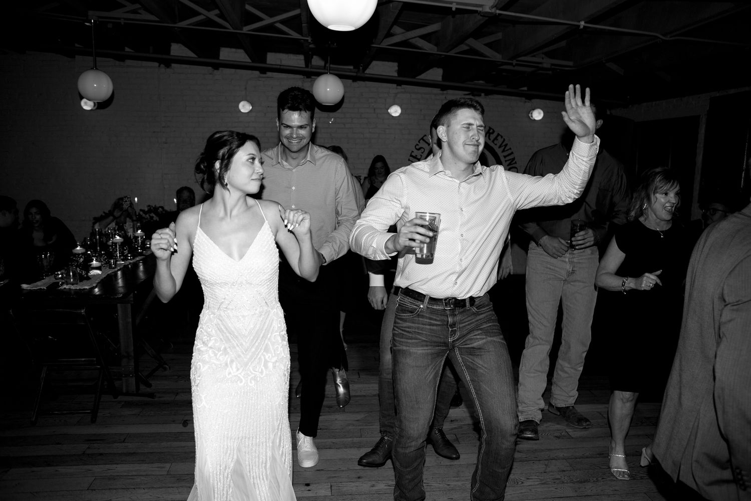 Guests dance energetically at a wedding reception in a casual venue.