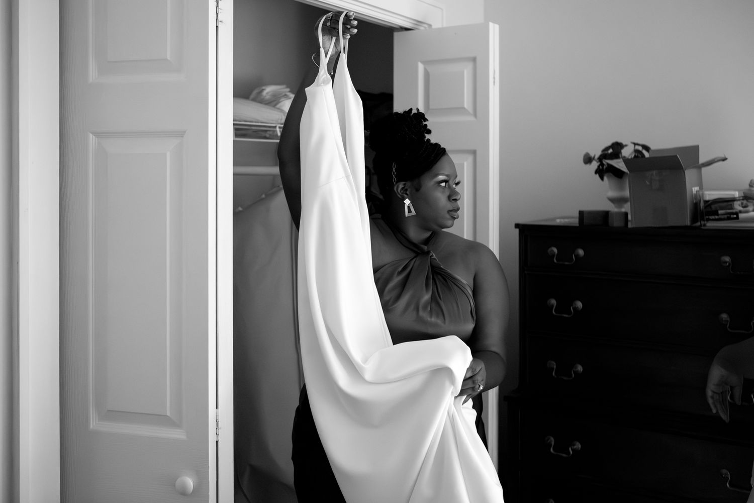 A person stands beside a white dress or garment hanging from a door in this black and white photograph.