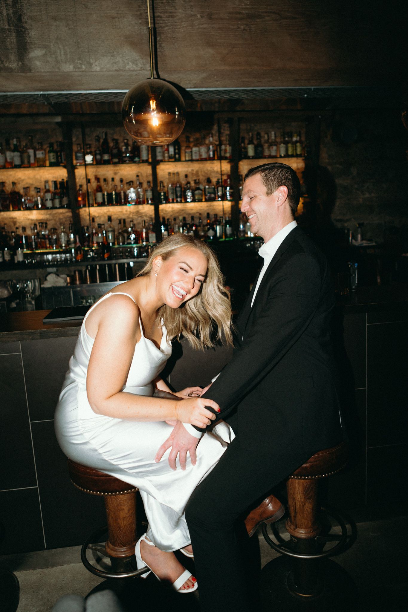 A couple shares an intimate moment at a dimly lit bar with vintage decor and bottles on display.