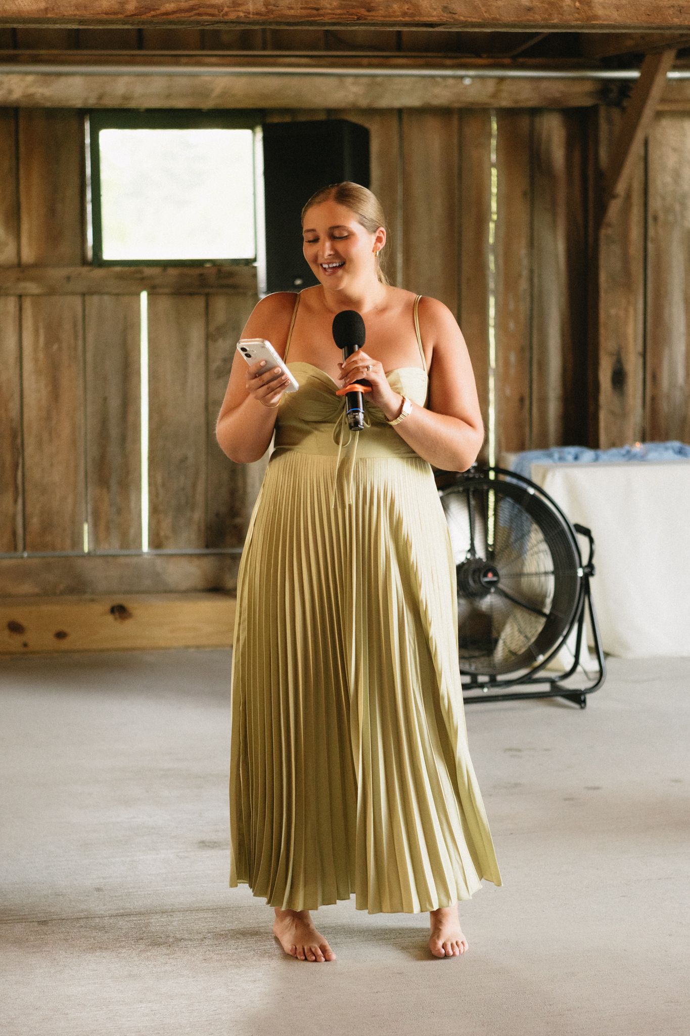 A woman in a flowing yellow pleated dress moves gracefully across a rustic wooden floor in a barn-like setting.