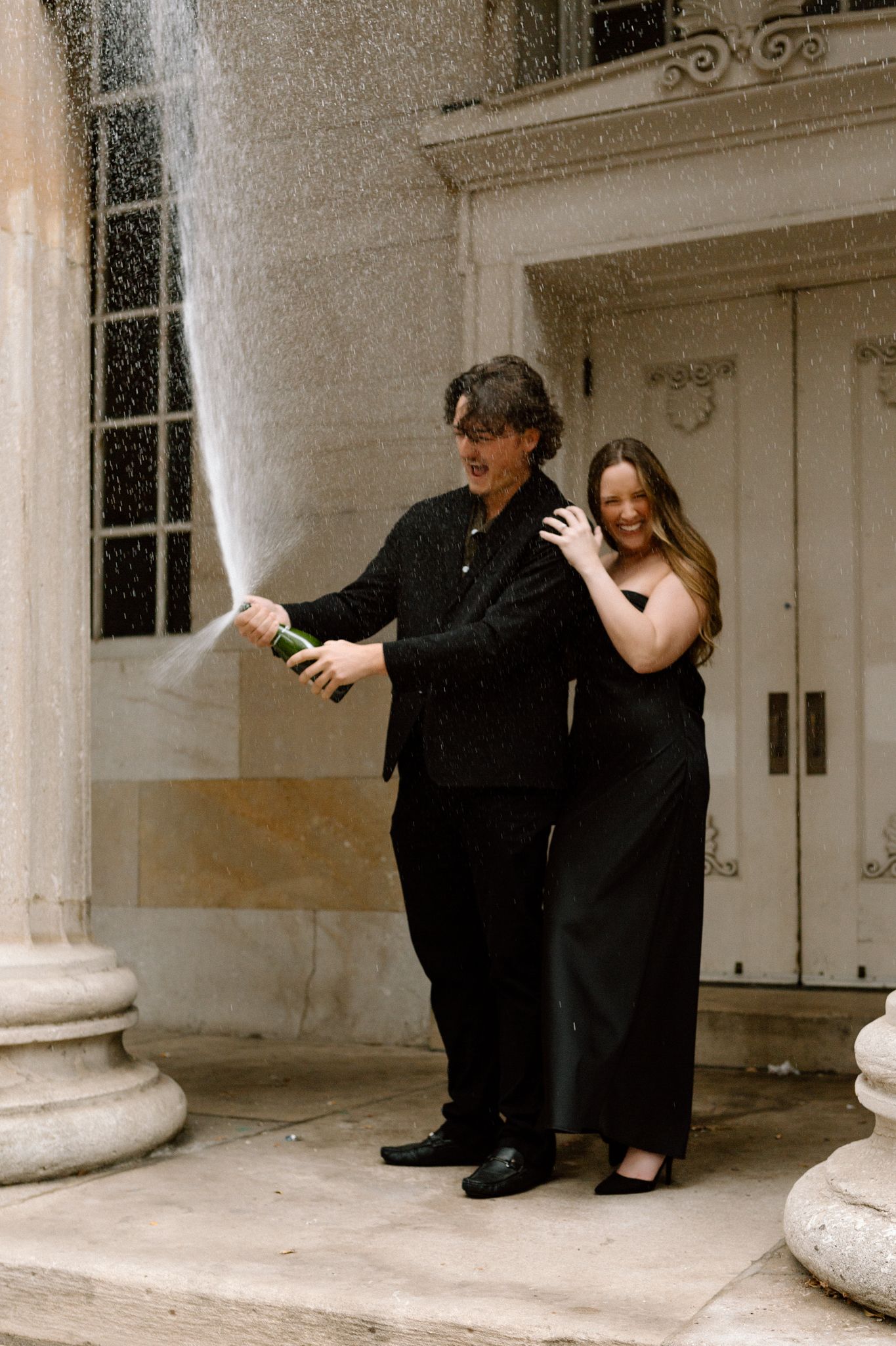 Engaged couple celebrating with a bottle of Chandon, sharing a joyful moment and laughter in downtown Louisville