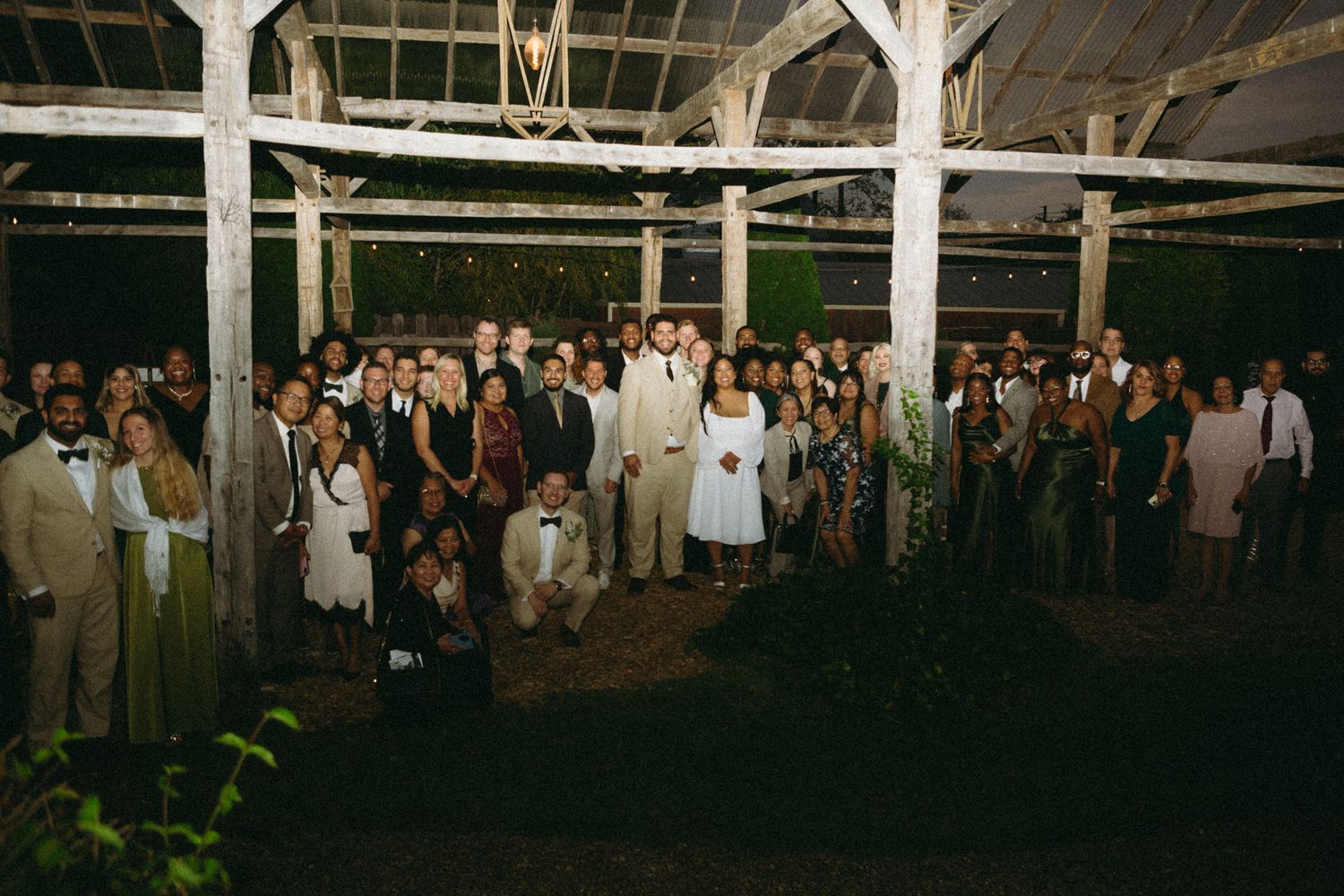 A group of people dancing and celebrating at night under string lights at an outdoor party.