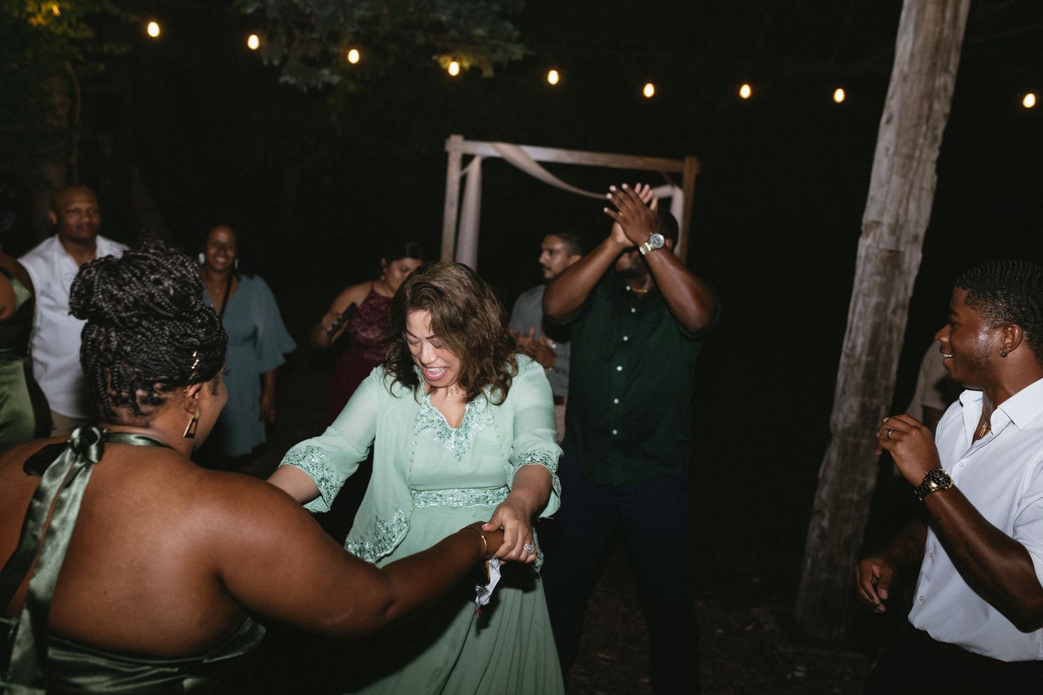 A group of people dancing and celebrating at night under string lights at an outdoor party.