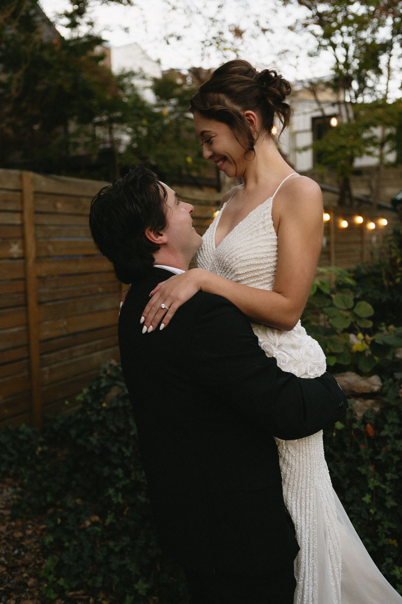A joyful wedding moment captured as the groom lifts his bride in an outdoor garden setting.
