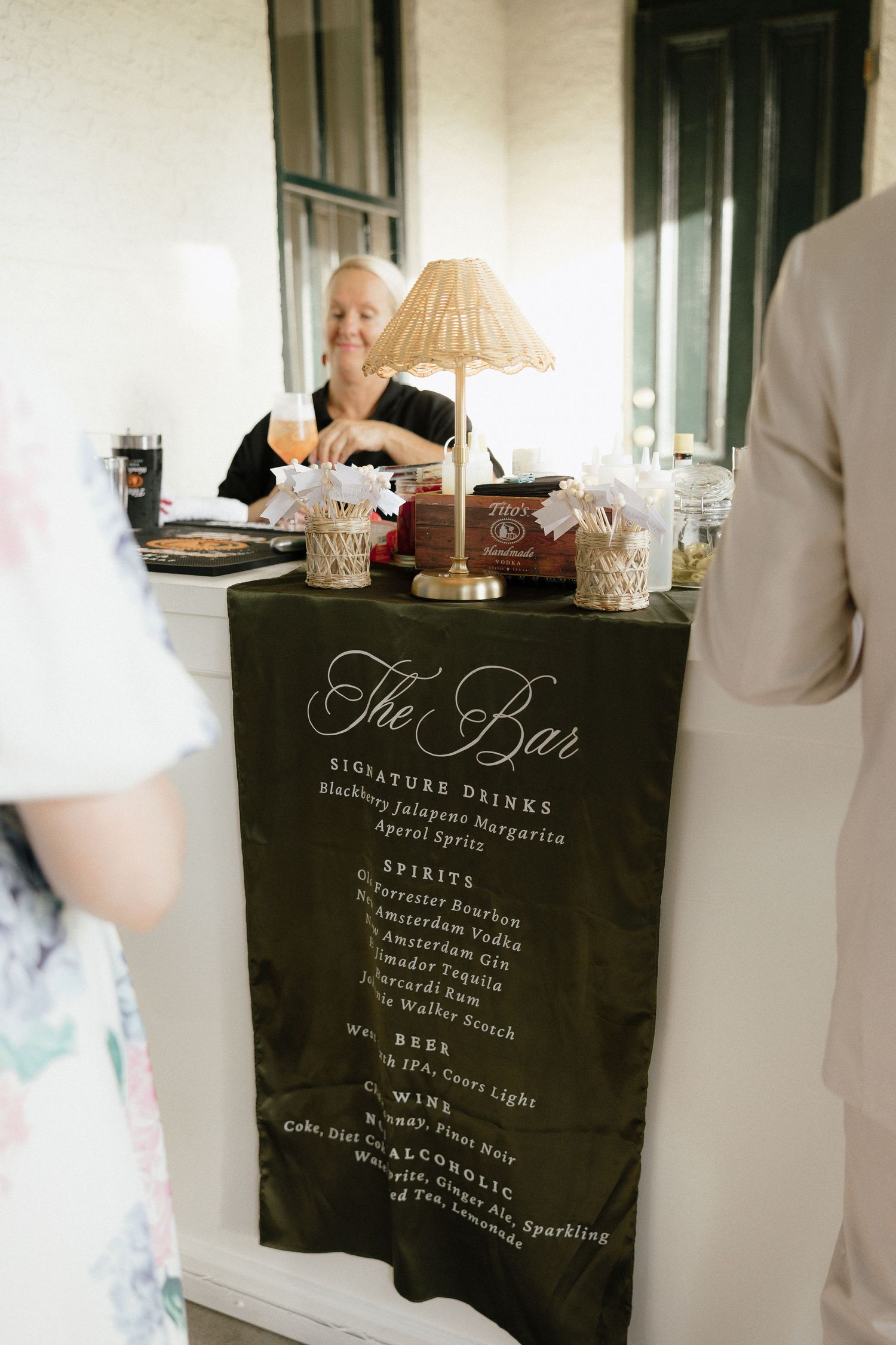 Elegant dark green wedding bar menu sign displays signature cocktails and spirits at a reception venue.