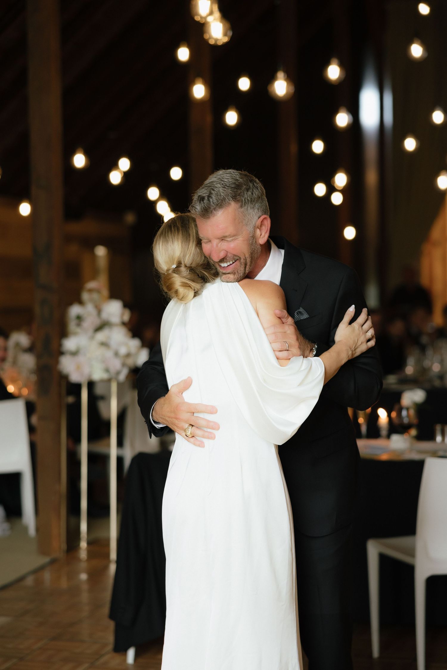 Couple shares a joyful embrace during first dance at romantic barn wedding reception.