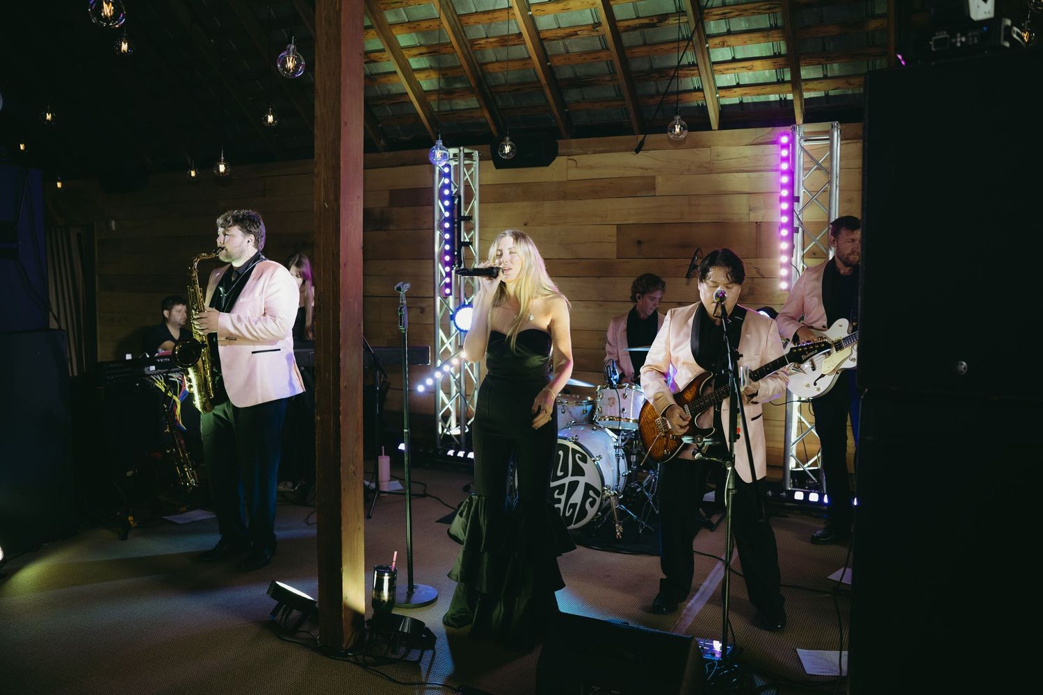 Live wedding band performing on stage with colorful lights in rustic barn reception venue.