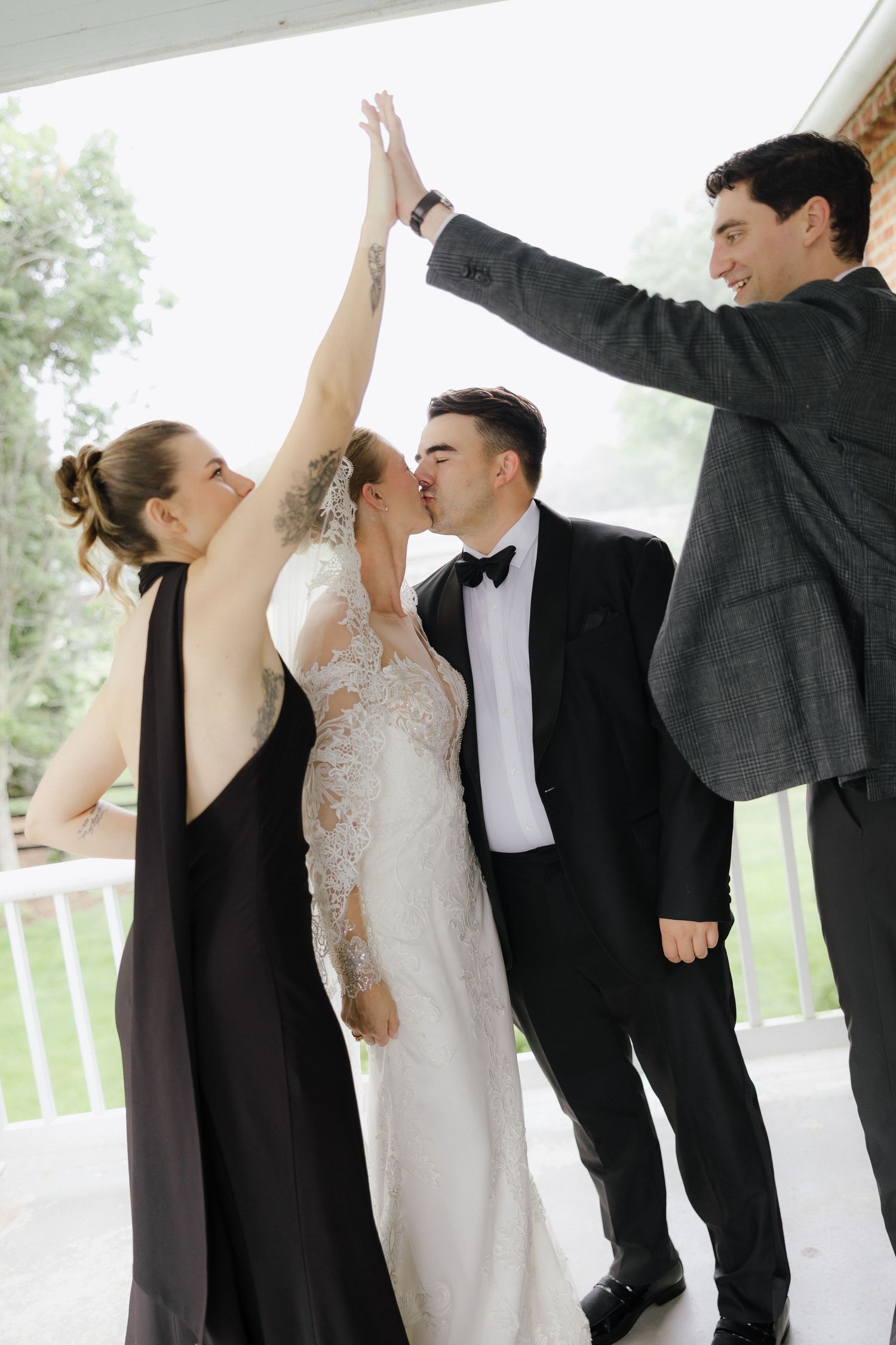Bride and groom kiss while wedding guests celebrate with high-fives during outdoor wedding reception.