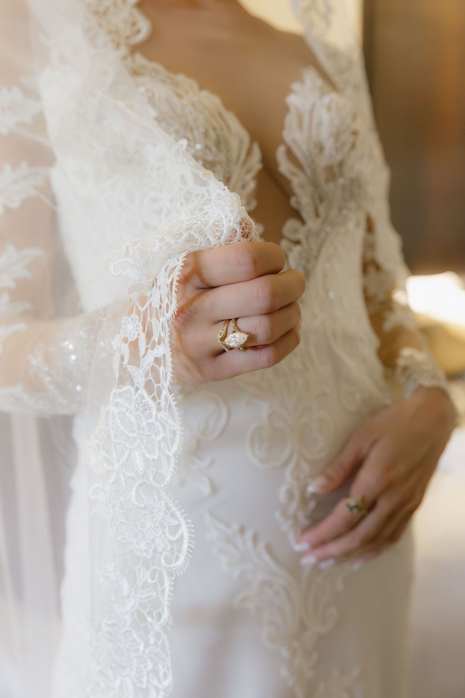 Close-up of bride in lace wedding gown displaying elegant gold diamond engagement ring and wedding band.