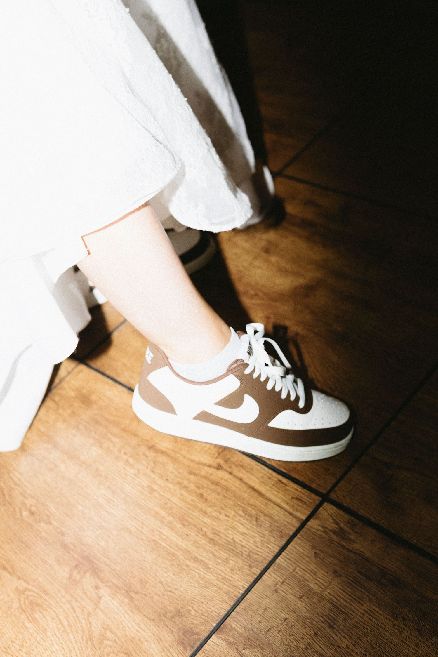 Close-up of sneakers worn with a wedding dress on a wooden floor.