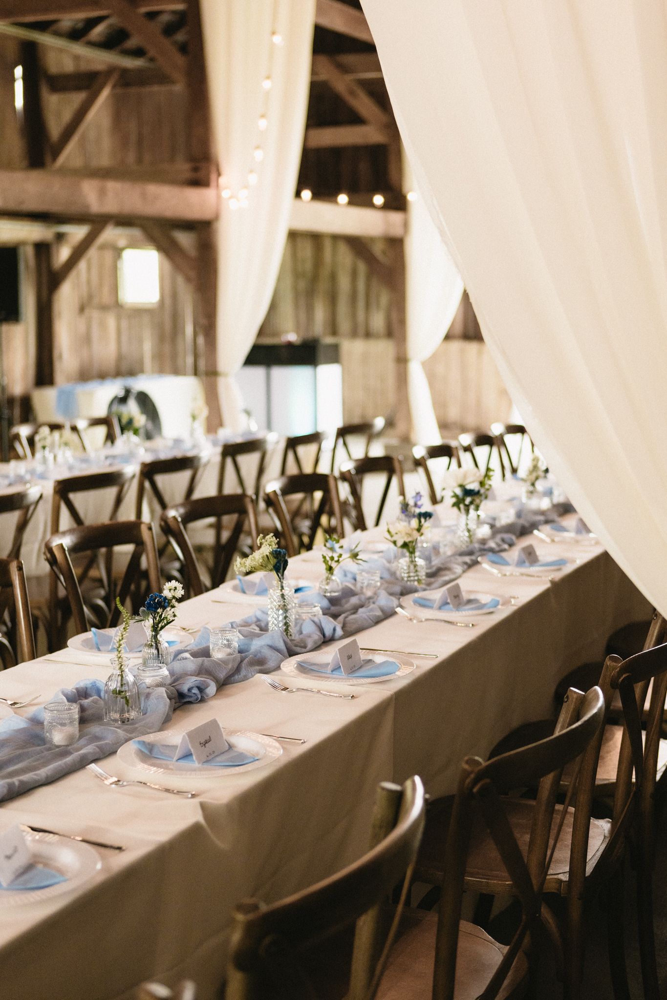Elegant wedding reception table setting in a barn with white drapes and place settings.
