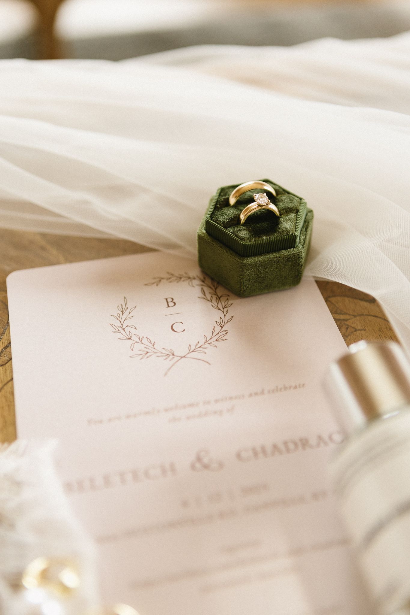 Wedding rings nestled in green velvet ring box on elegant invitation card with silk ribbon details.