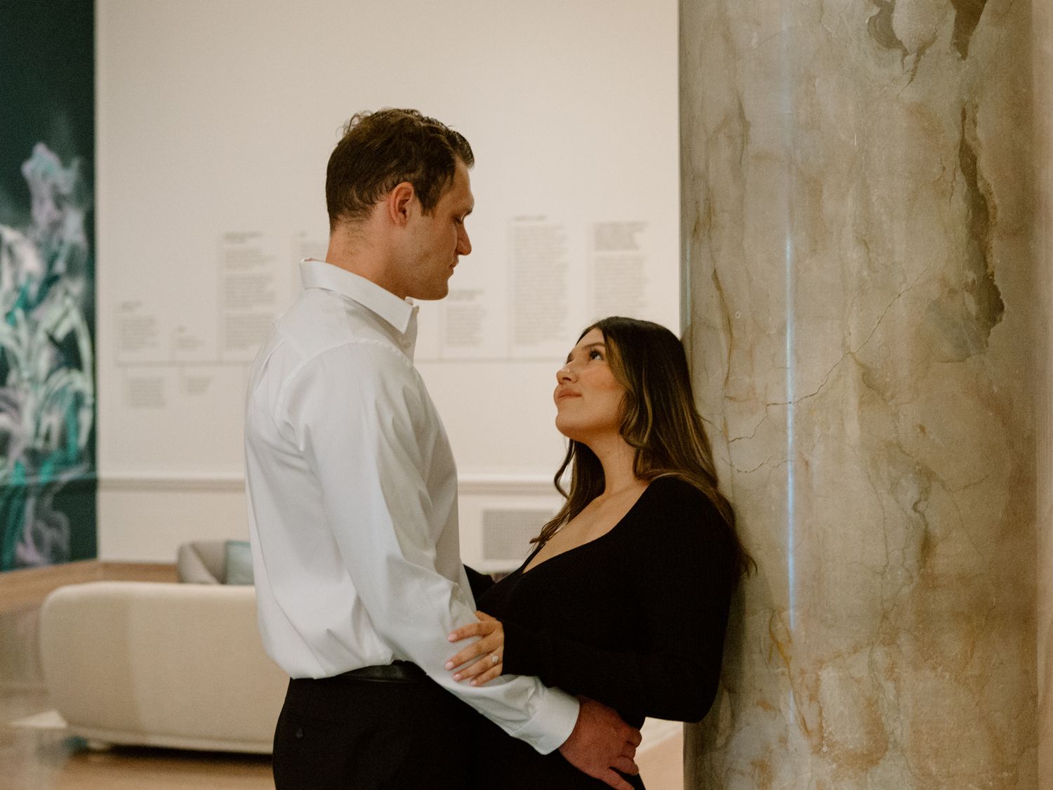 Elegant engaged couple smiling and embracing in downtown Louisville, with the woman showing her engagement ring
