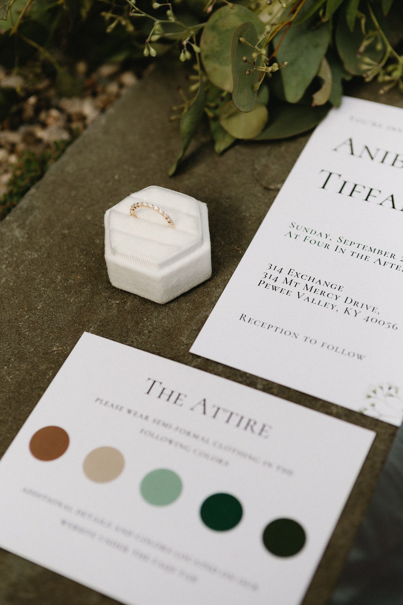 Wedding invitation details with color palette swatches and a white hexagonal ring box on a stone surface.