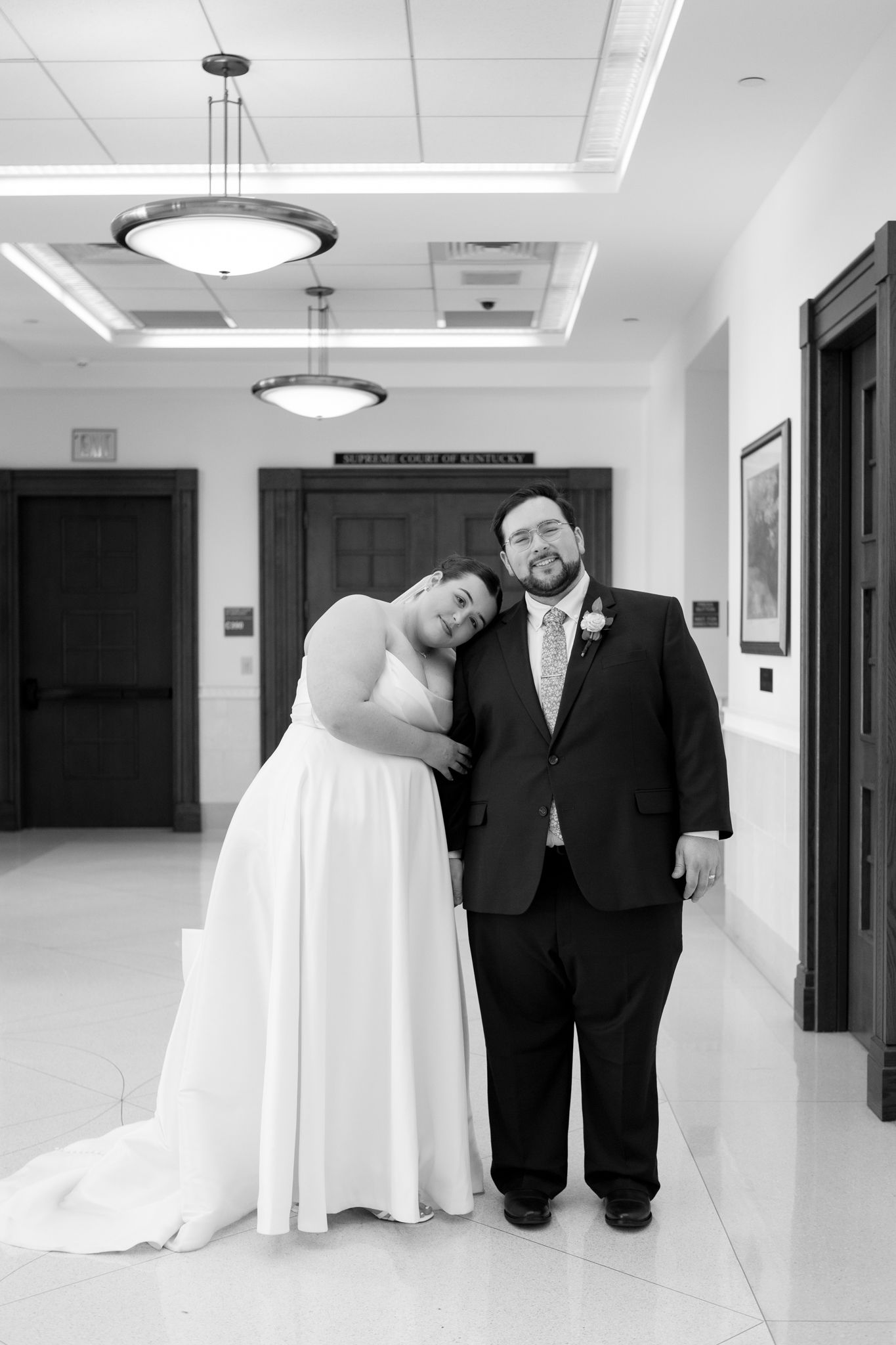 A wedding couple walks together down a bright white hallway with modern lighting fixtures.
