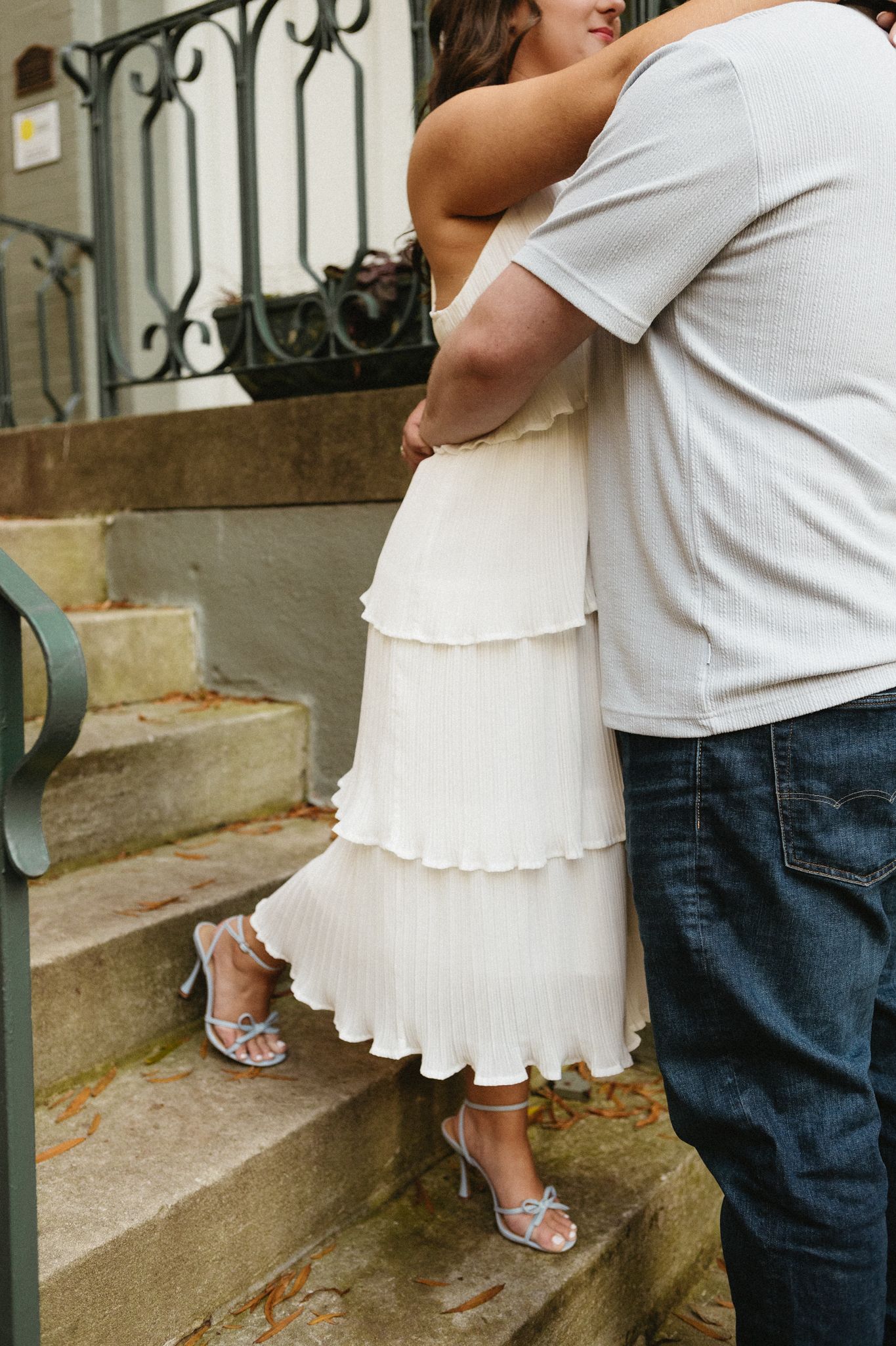 Two people embracing on concrete steps wearing white and denim outfits.