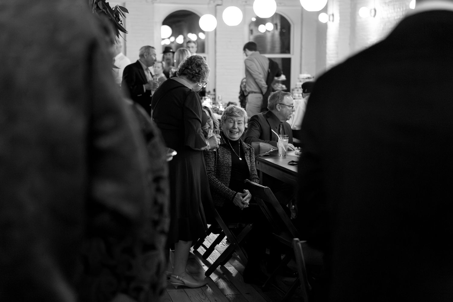 A candid black and white shot of wedding guests gathered in a dimly lit reception venue.