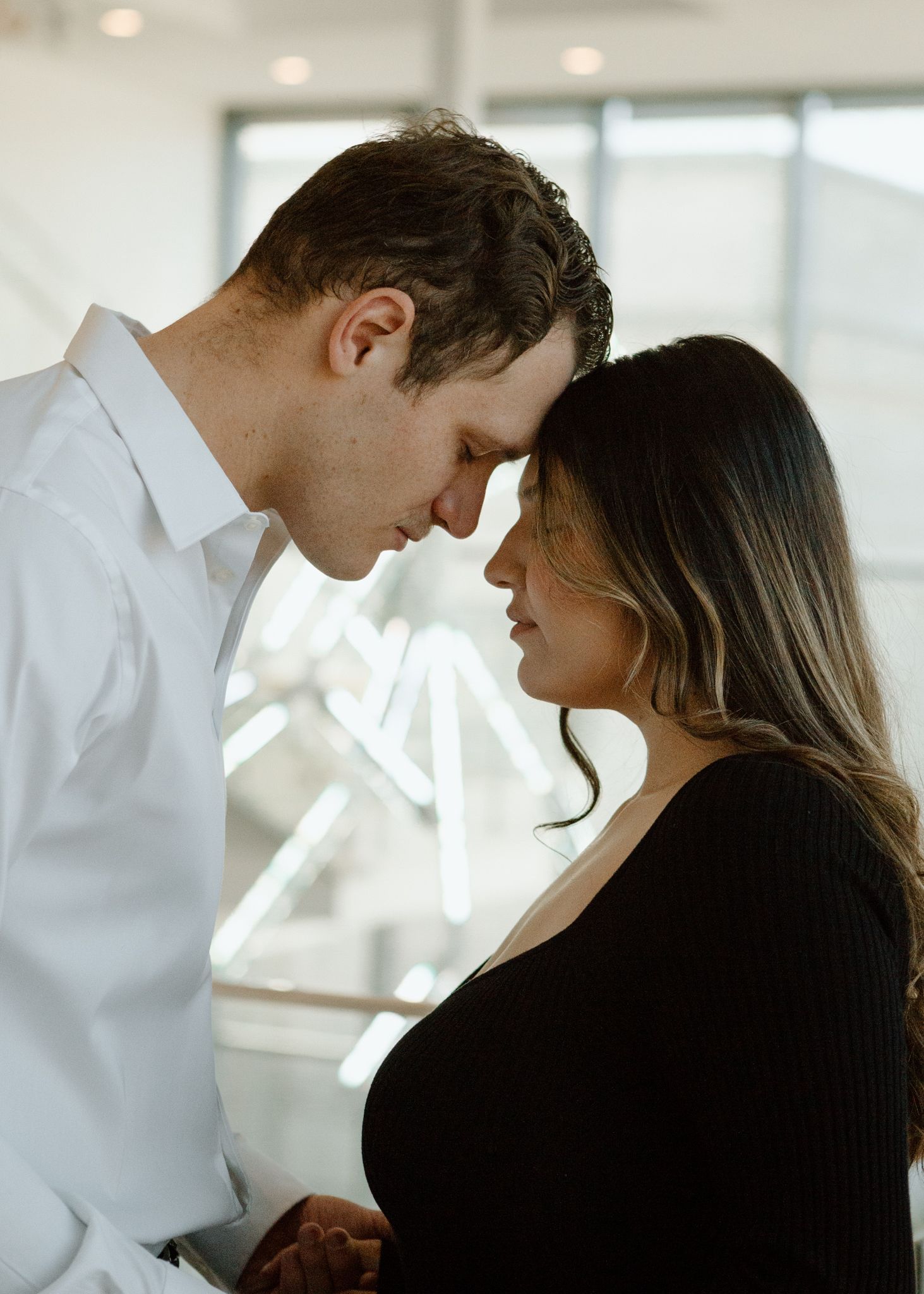Engaged couple in downtown Louisville, with the woman smiling and showing her engagement ring while embracing her fiancé