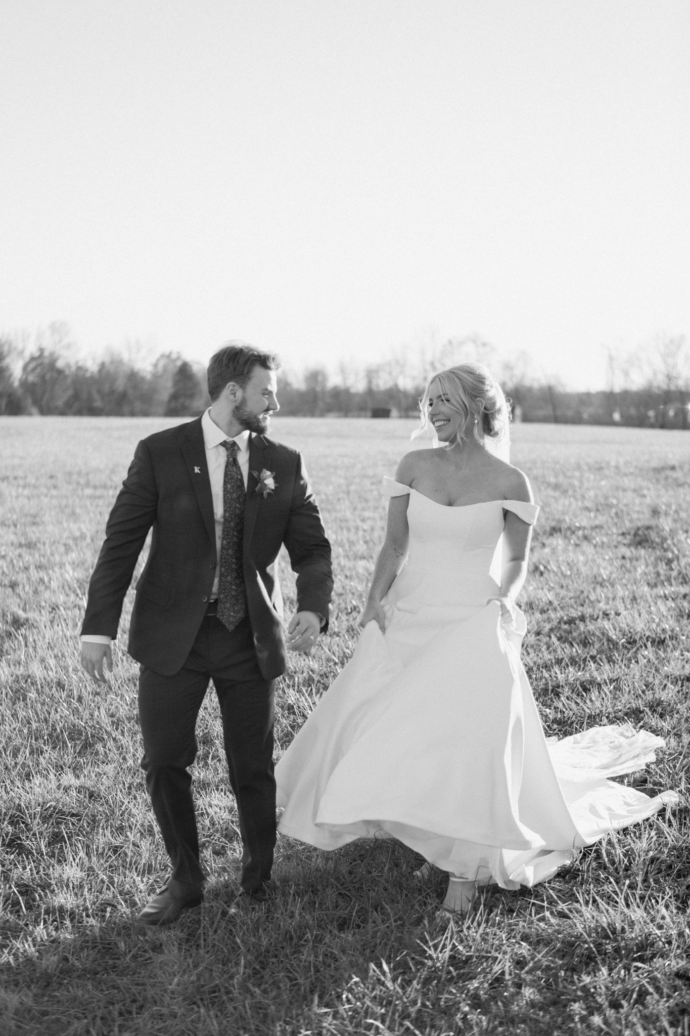 Bride and groom walking through a sunny field at Silo Farms, captured in black and white. Photo by Joia Lyn, KY wedding