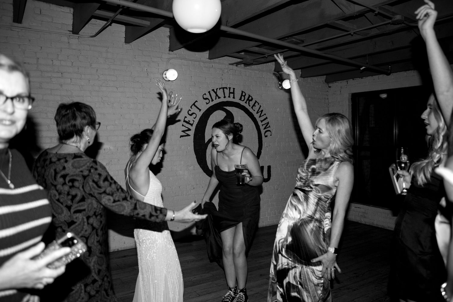 Black and white photo of people dancing and celebrating at an indoor party with string lights.