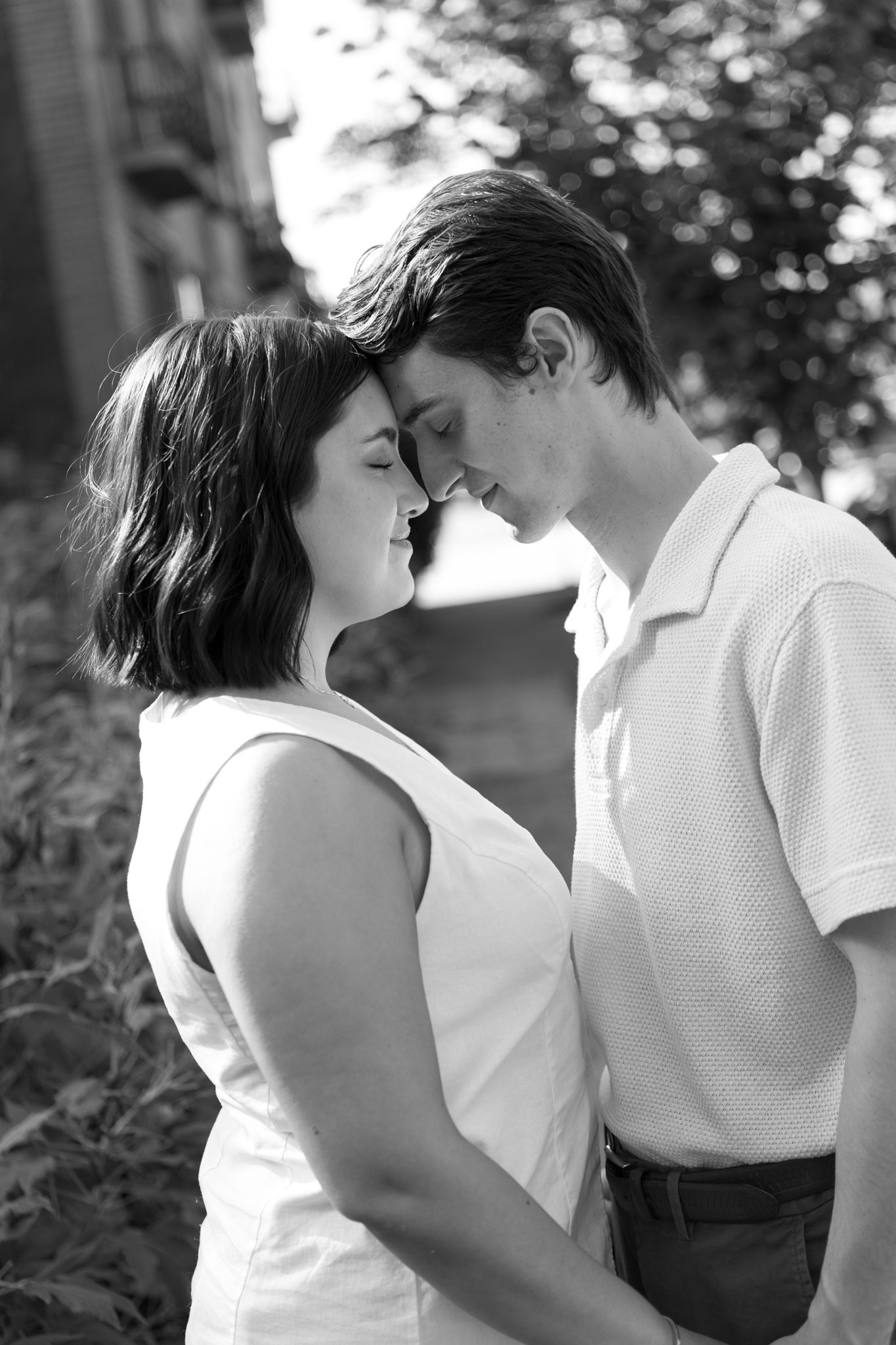 A black and white portrait of a couple sharing a romantic moment outdoors.