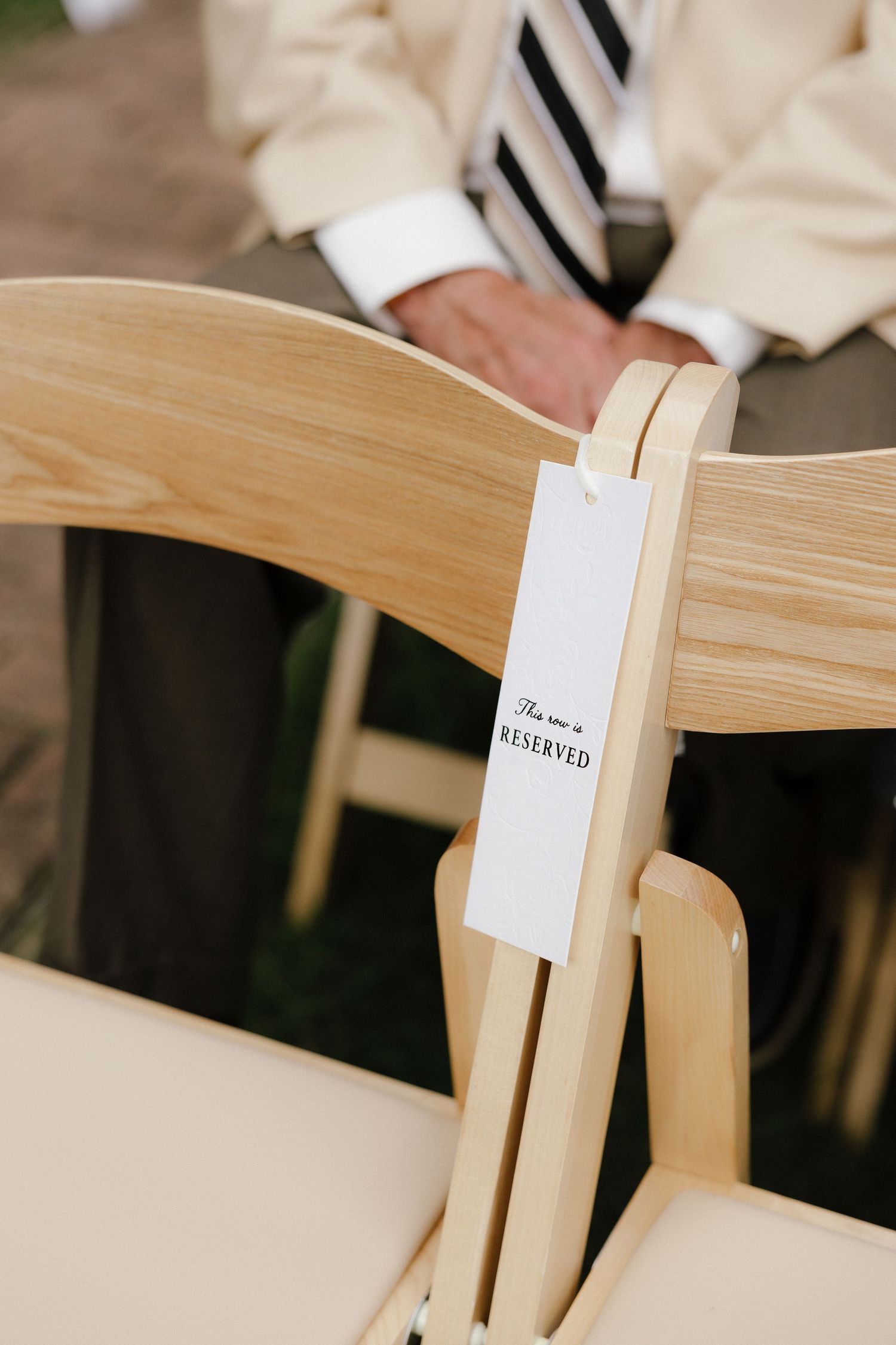 Wooden folding chair with white reserved tag at an elegant outdoor wedding ceremony.